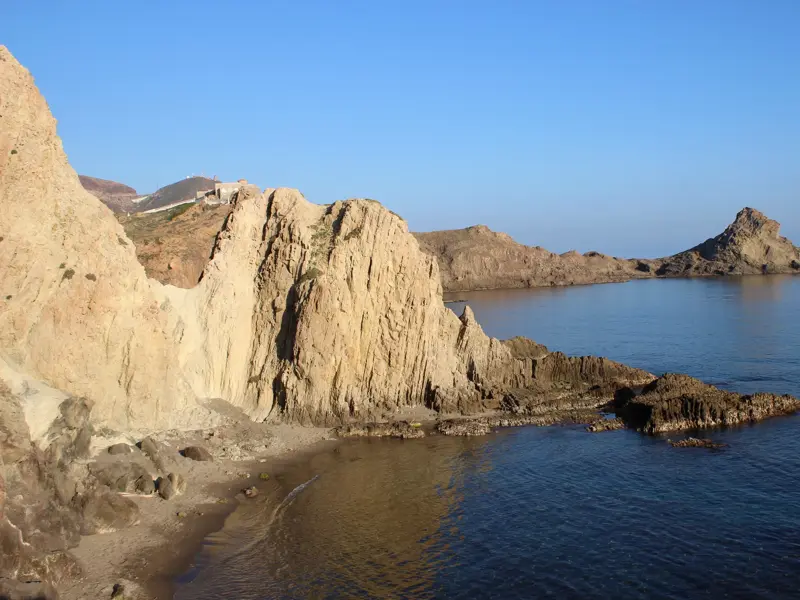 Schroffe, sonnenbeschienene Felsklippen und eine kleine Bucht an der Küste des Naturparks Cabo de Gata in Andalusien.