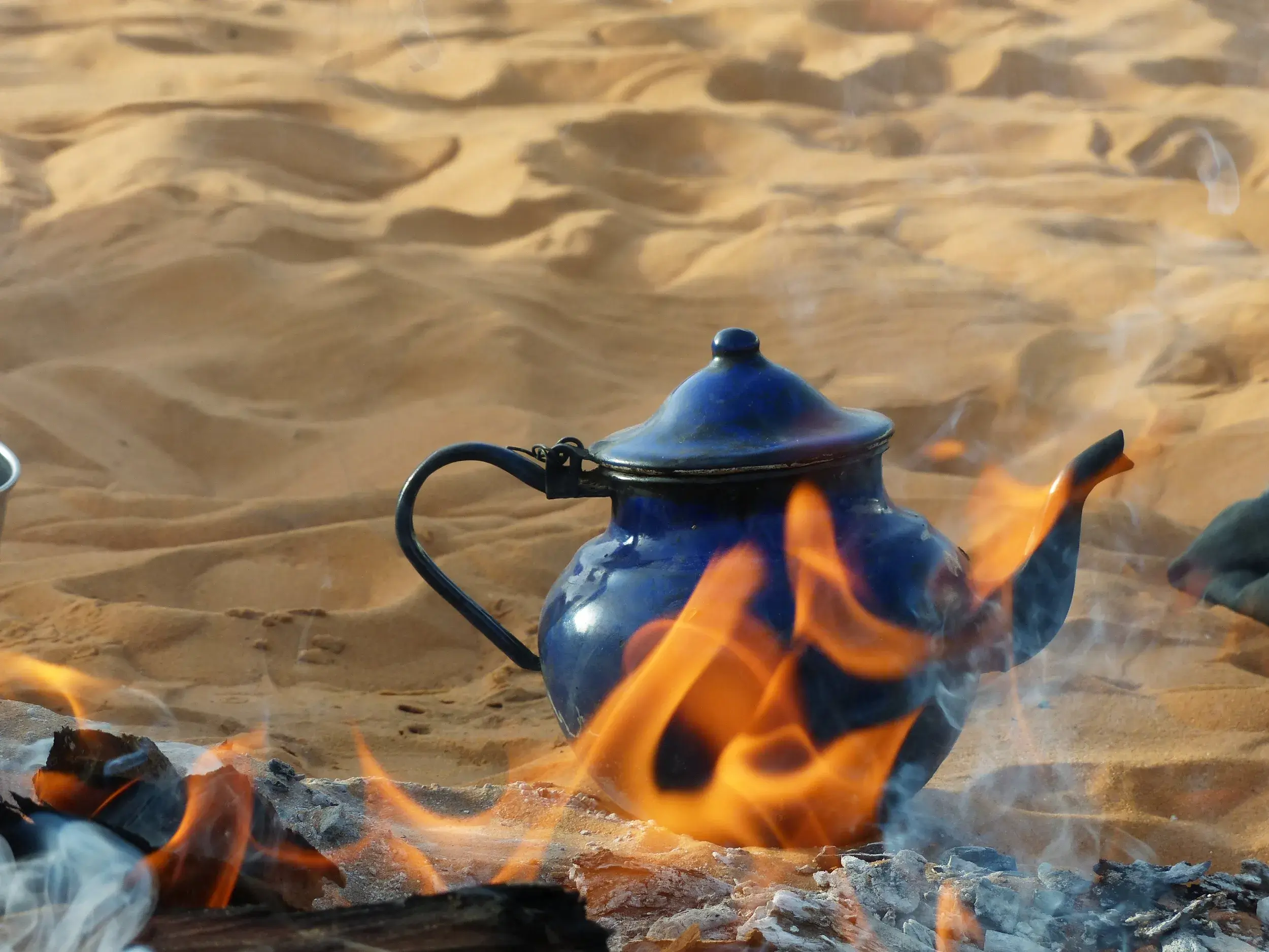 Traditionelle Teezeremonie mit einer blauen Kanne auf dem Lagerfeuer während eines Wüstentrekkings in der Sahara Marokkos.