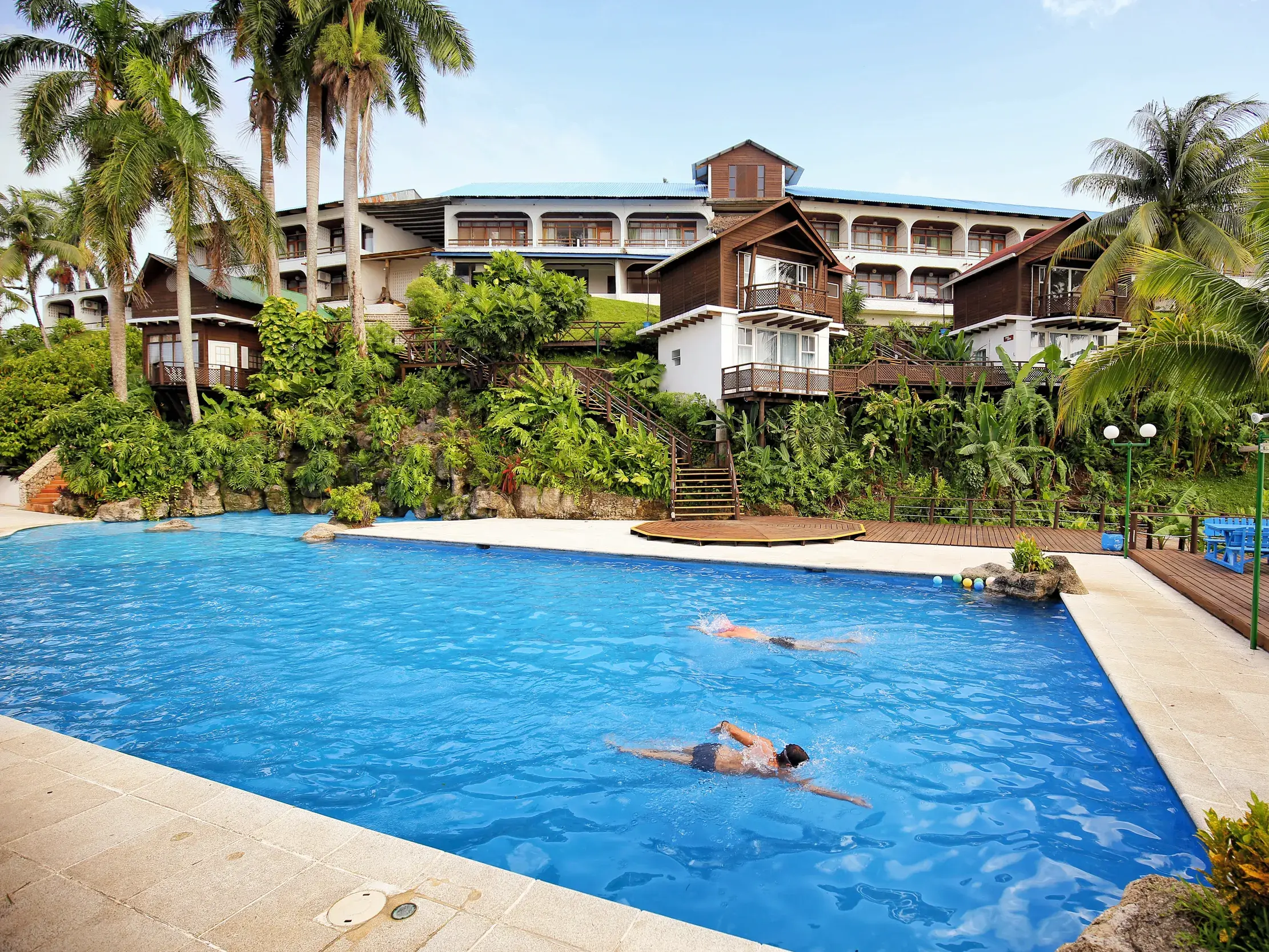 Pool des Hotels Villa Maya in Livingston an der Karibikküste Guatemalas mit zwei schwimmenden Gästen und einer von Palmen gesäumten Anlage.