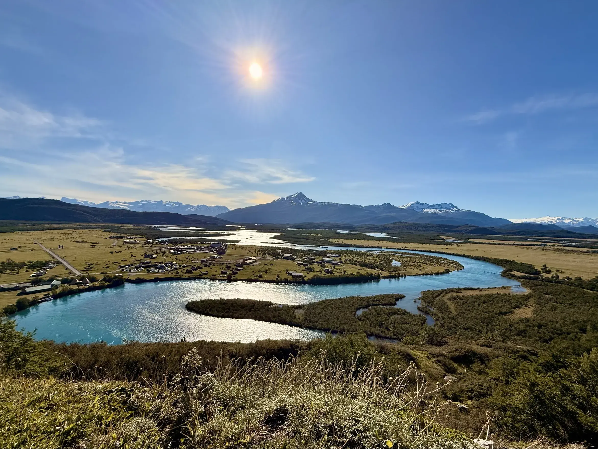 Blick vom Aussichtsberg Cerro del Medio auf einen türkisen Fluss im weiten Tal von Feuerland unter sonnigem Himmel.