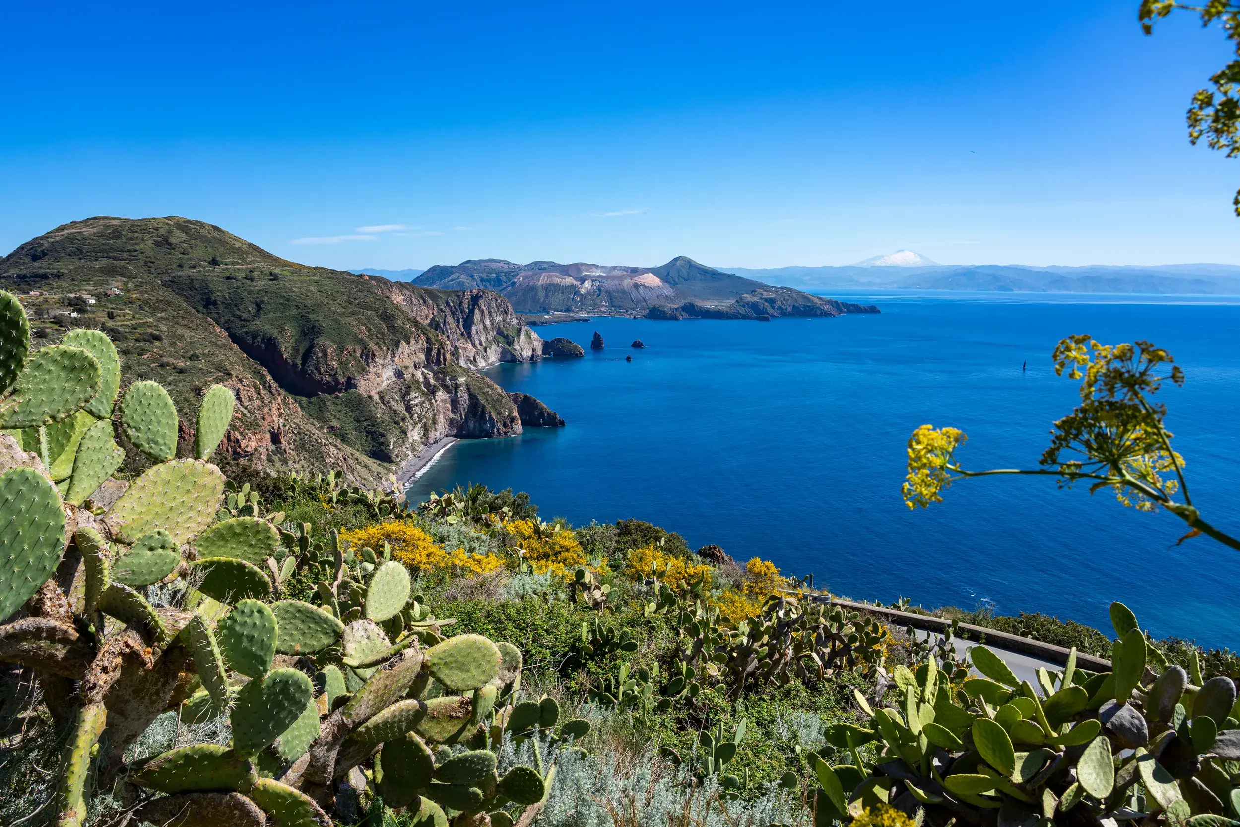 Aussicht bei einer Wanderung auf den Äolischen Inseln über die Steilküste und das Meer zur Insel Vulcano und dem Ätna.