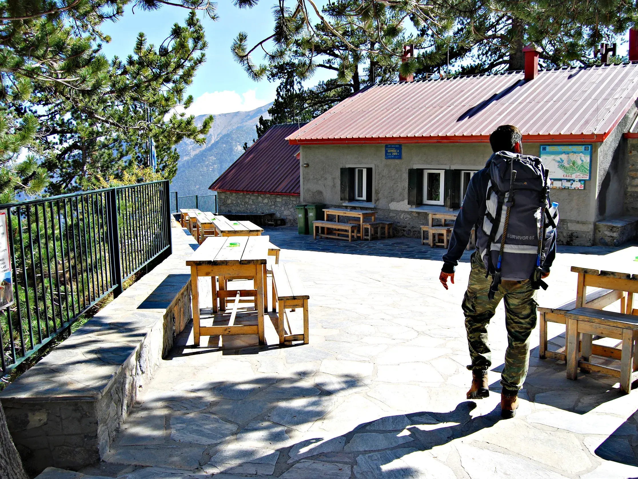 Ein Wanderer mit Trekkingrucksack erreicht die Berghütte Spilios Agapitos im Olymp-Massiv an einem sonnigen Tag.