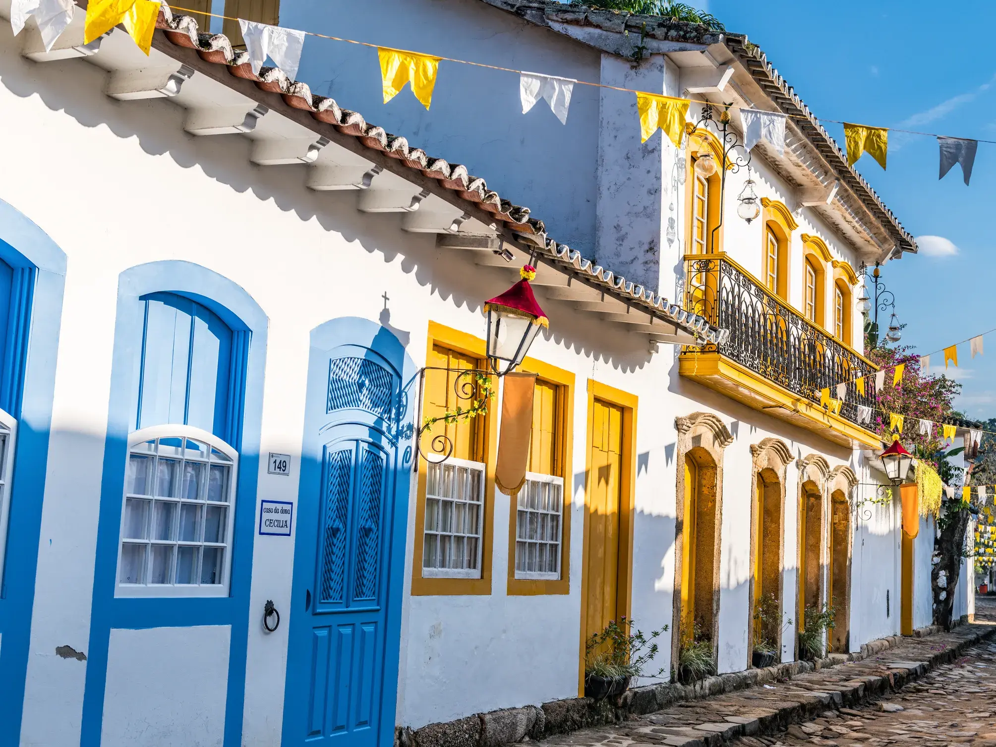 Sonnige Kopfsteinpflastergasse in Paraty mit weißen Kolonialhäusern, bunten Türen und festlichen Wimpelketten.