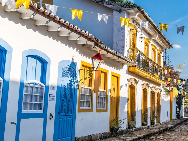 Sonnige Kopfsteinpflastergasse in Paraty mit weißen Kolonialhäusern, bunten Türen und festlichen Wimpelketten.
