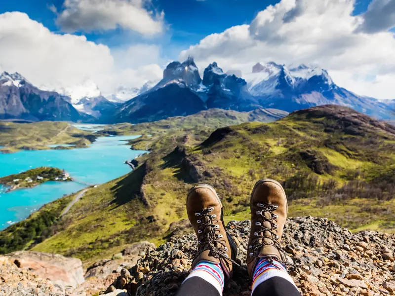 Wanderer macht eine Pause und blickt von einem Felsen auf den türkisen Lago Pehoé und die Cuernos del Paine in Chile.
