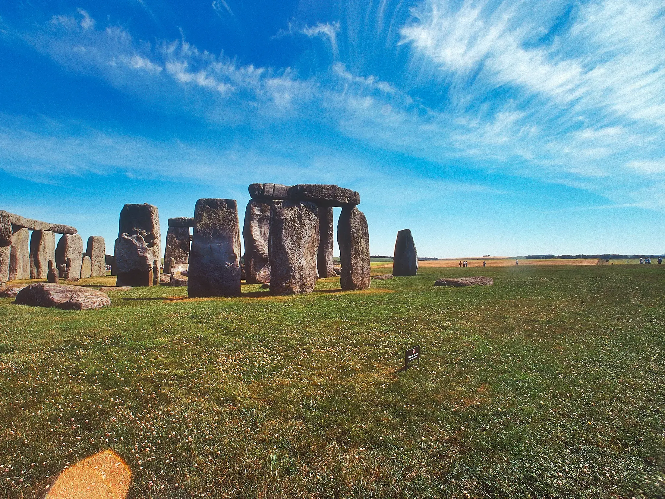 Der berühmte Steinkreis Stonehenge, ein UNESCO-Welterbe, auf einer weiten Wiese unter blauem Himmel in Südengland.