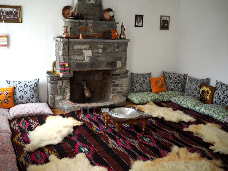Traditionelle Sitzecke mit Kissen und Schaffellen am Steinkamin in einem albanischen Homestay während der Trekkingreise.
