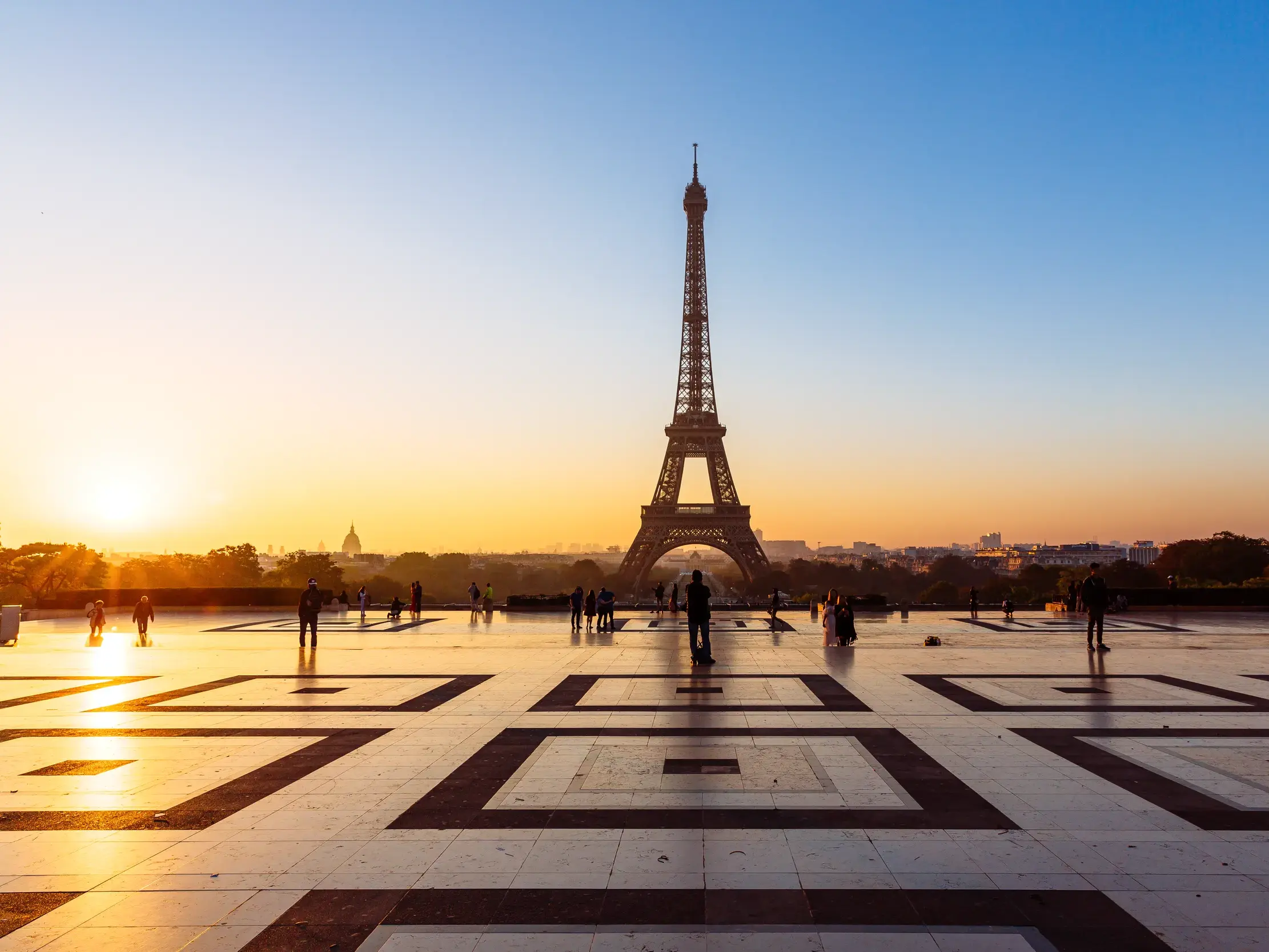 Goldenes Morgenlicht beleuchtet den Eiffelturm und die Skyline von Paris, gesehen vom Trocadéro-Platz mit Passanten.