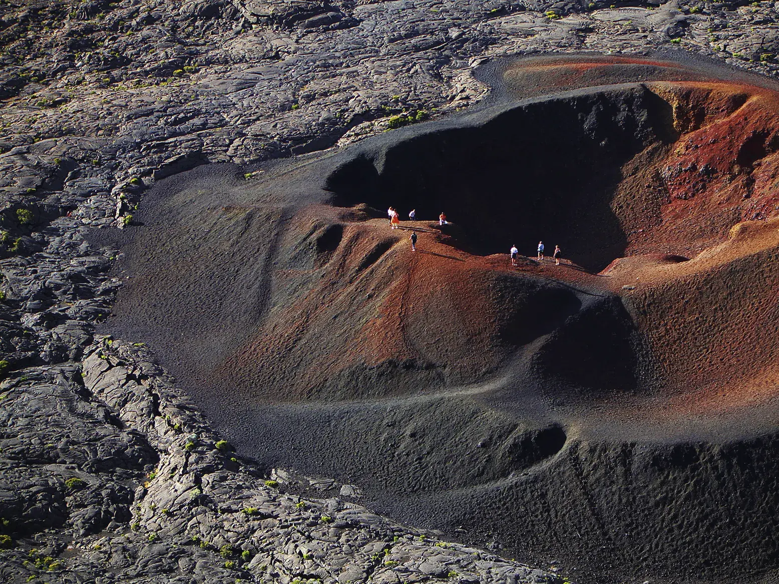 Eine kleine Wandergruppe wandert auf dem rot-schwarzen Kraterrand des Formica Leo in der Vulkanlandschaft des Piton de la Fournaise.