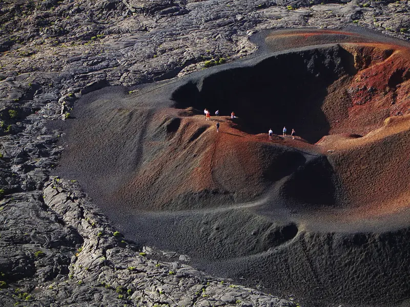 Eine kleine Wandergruppe wandert auf dem rot-schwarzen Kraterrand des Formica Leo in der Vulkanlandschaft des Piton de la Fournaise.