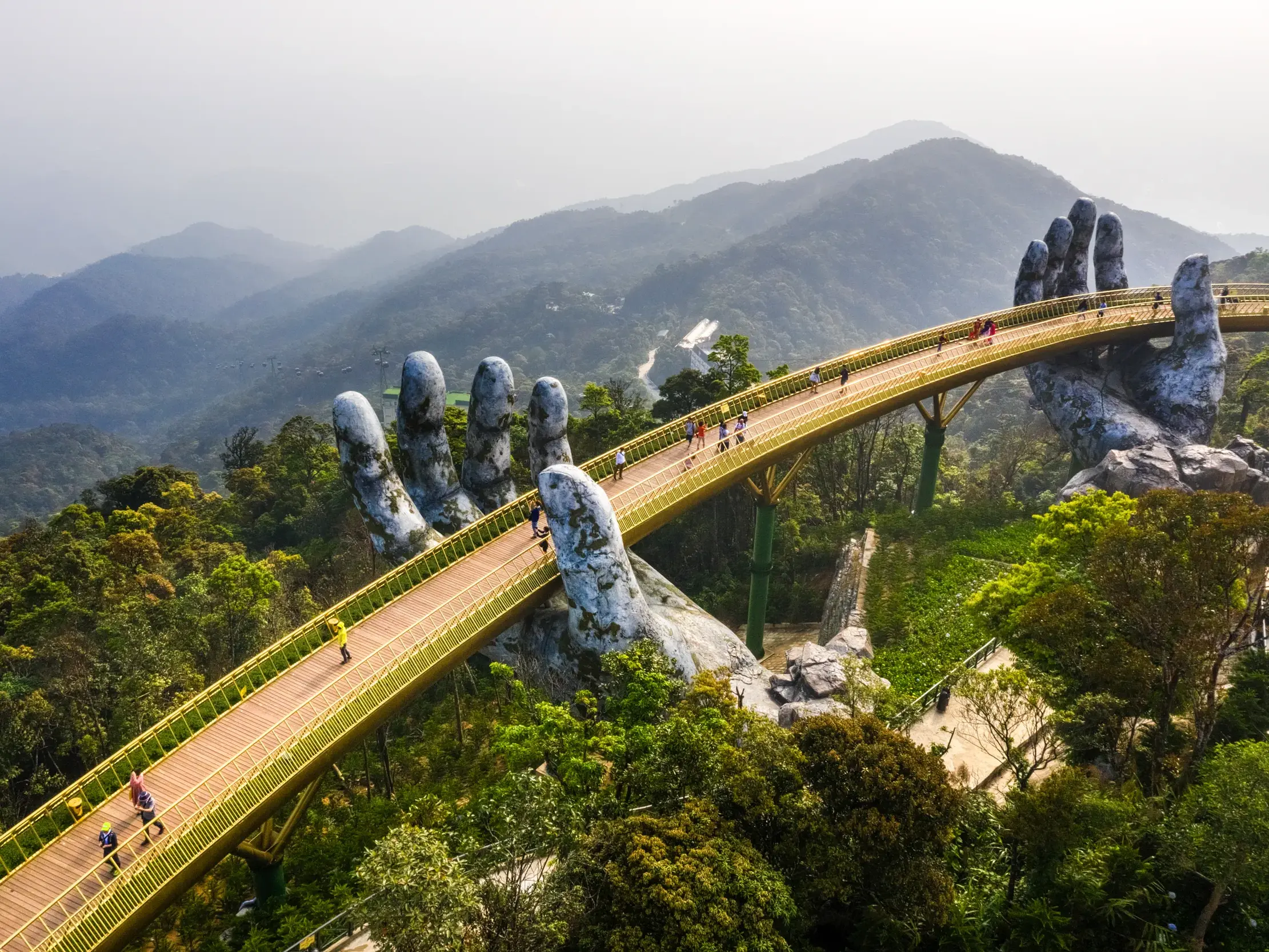 Junge Reisende überqueren die berühmte Goldene Brücke in Vietnams Ba Na Hills, die von zwei riesigen Steinhänden gehalten wird.
