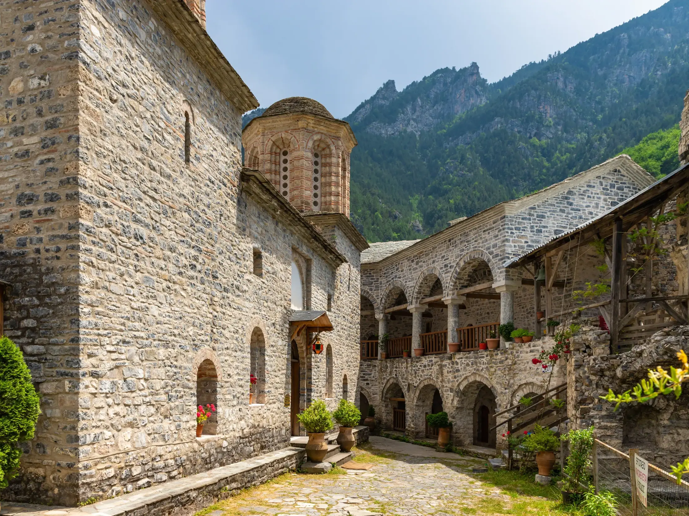Innenhof des historischen Klosters Agios Dionysios am Olymp mit Steinarkaden vor der bewaldeten Bergkulisse Griechenlands.