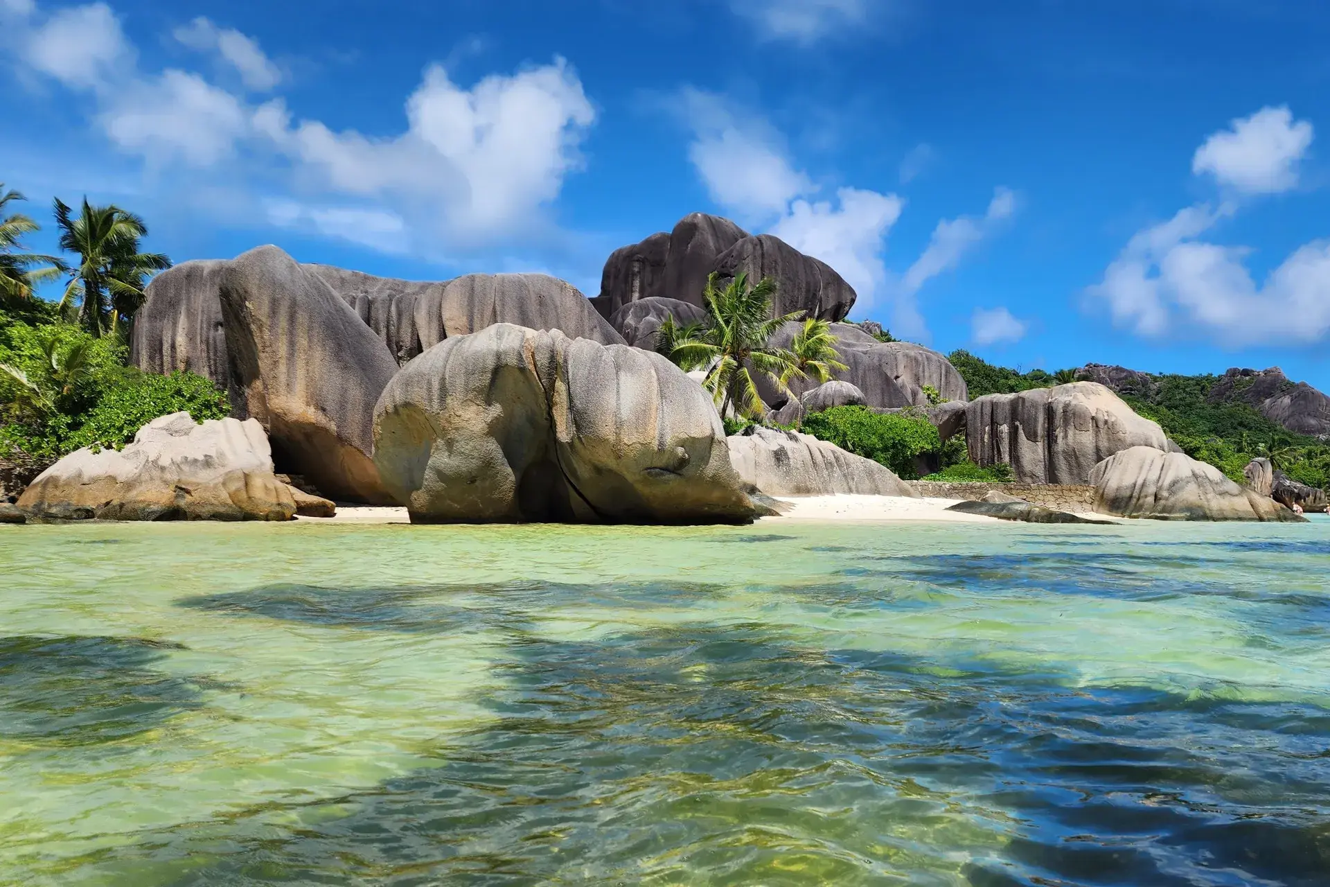 Blick vom Wasser auf die markanten Granitfelsen und Palmen am Traumstrand Anse Source d'Argent auf La Digue, Seychellen.