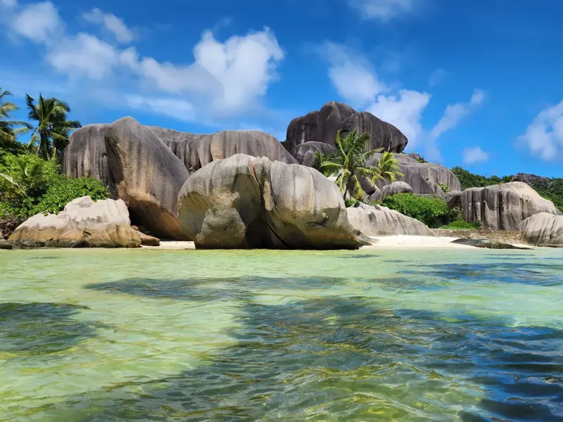 Blick vom Wasser auf die markanten Granitfelsen und Palmen am Traumstrand Anse Source d'Argent auf La Digue, Seychellen.