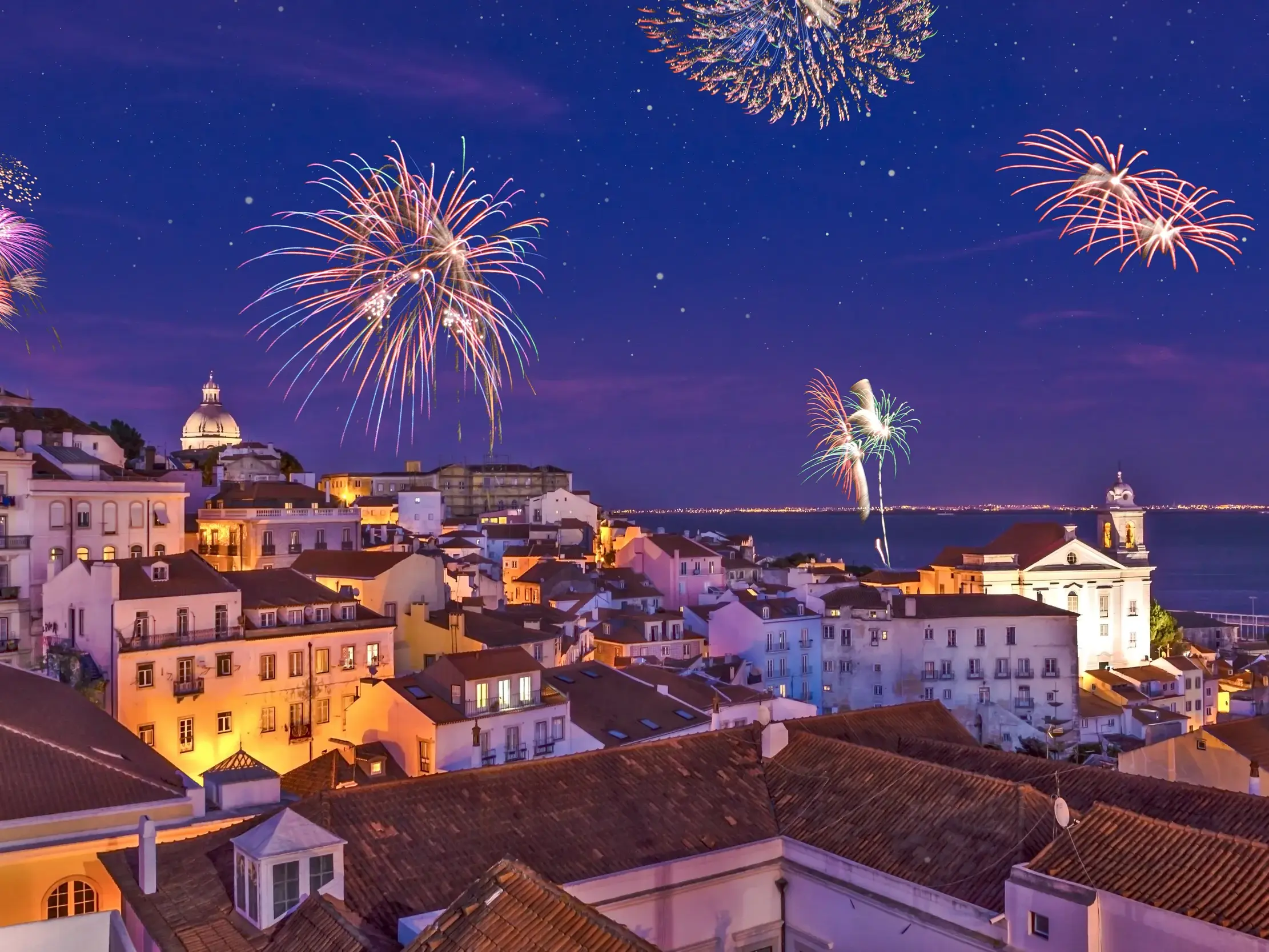 Festliches Neujahrsfeuerwerk erleuchtet den Nachthimmel über der historischen Altstadt von Lissabon mit Blick auf den Tejo.
