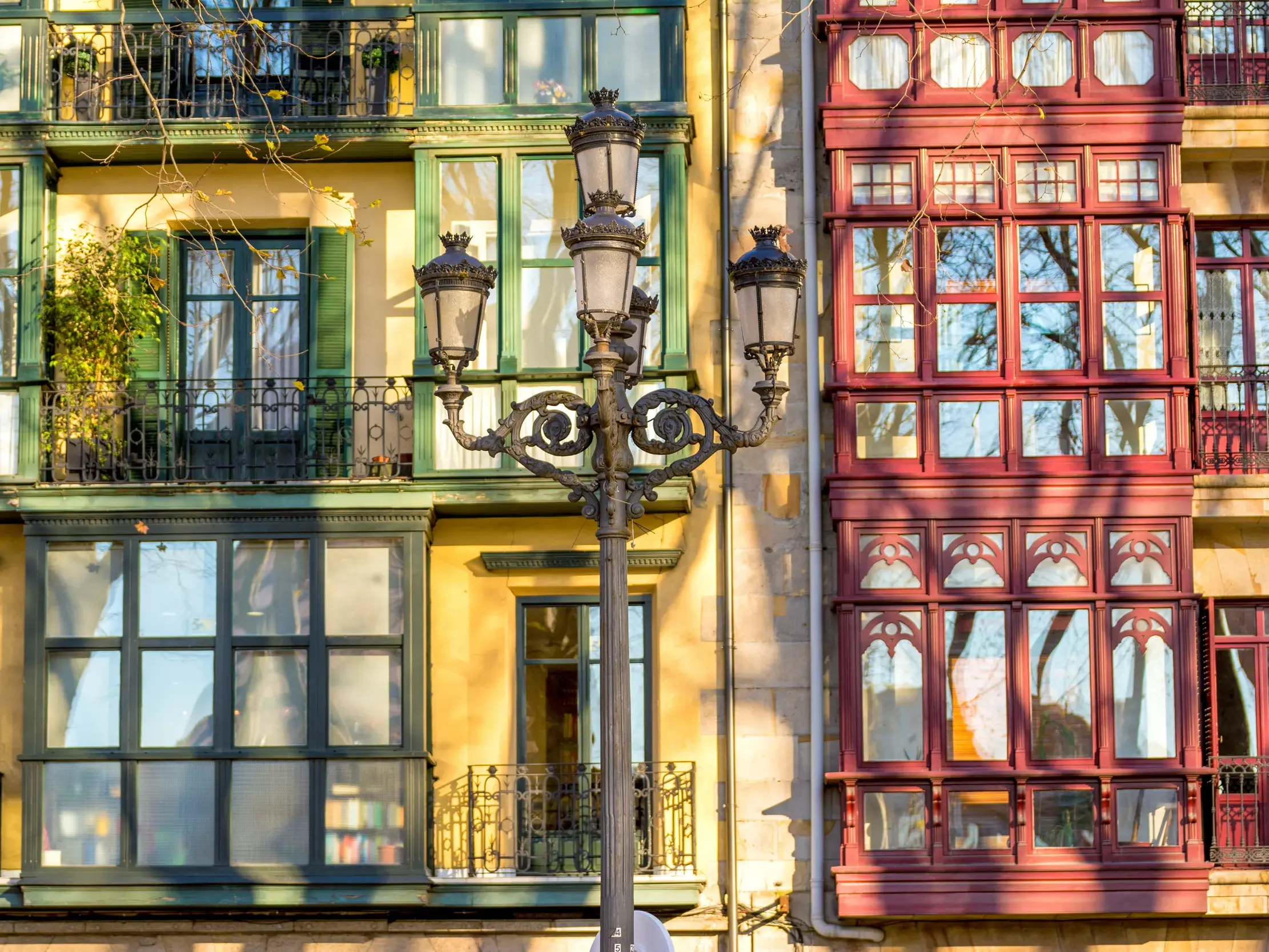 Eine verzierte Straßenlaterne vor bunten Hausfassaden mit typischen Erkerfenstern in der Altstadt von Bilbao.