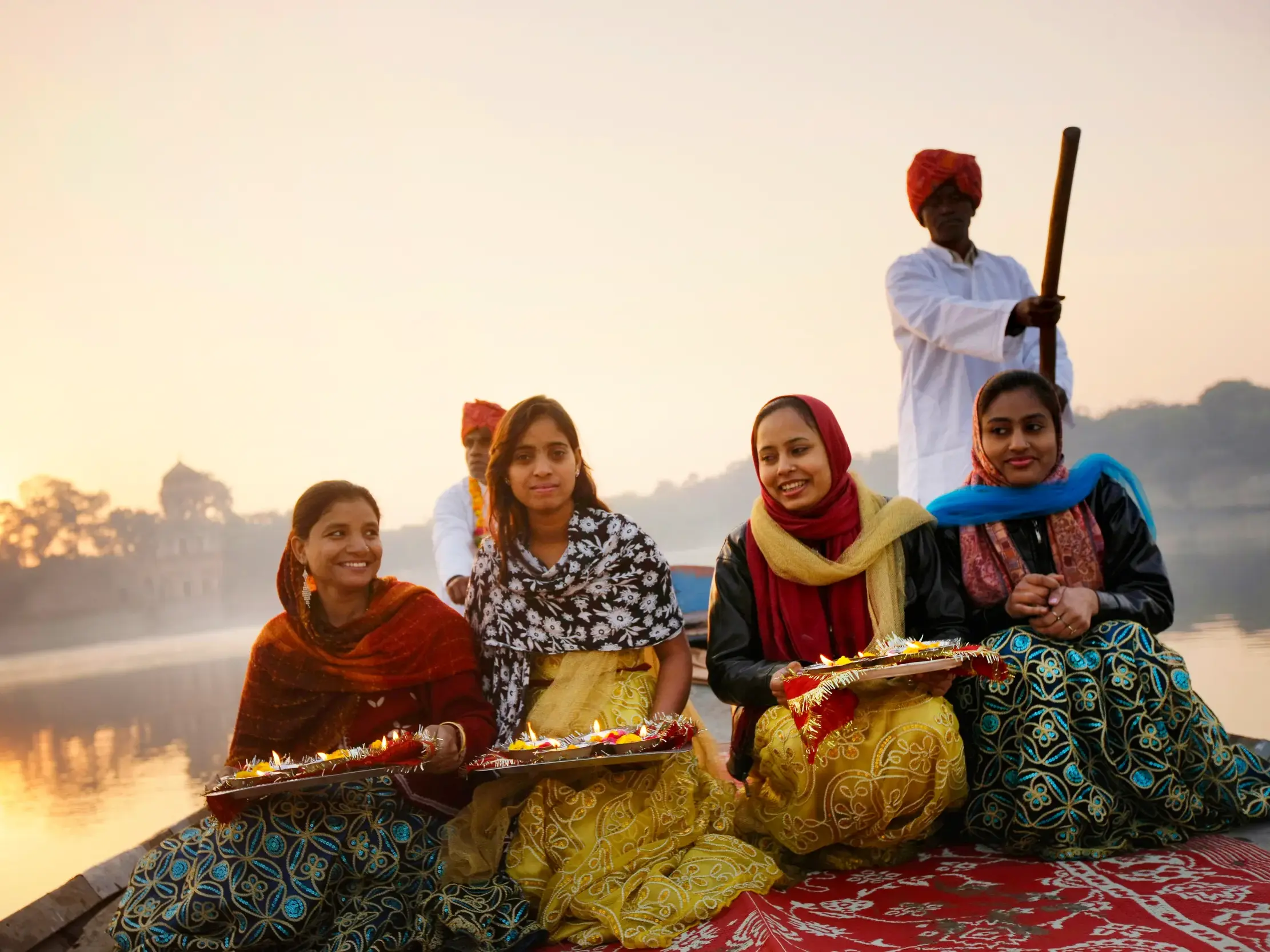 Vier indische Frauen mit Opferschalen auf einer Bootsfahrt bei Sonnenaufgang auf dem Picholasee in Udaipur, Rajasthan.