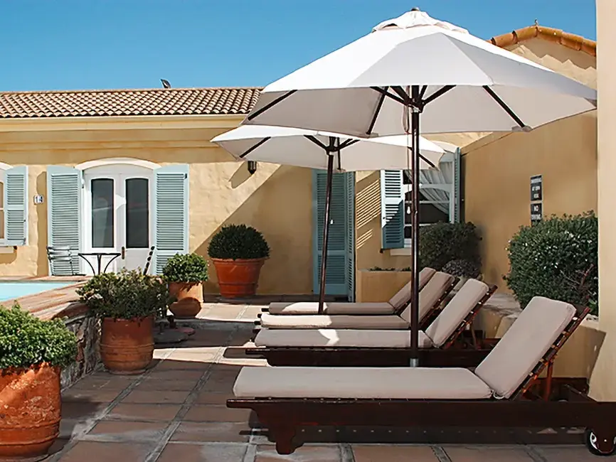 Sonnige Poolterrasse der Auberge Burgundy in Hermanus mit bequemen Liegen und weißen Sonnenschirmen zum Entspannen.