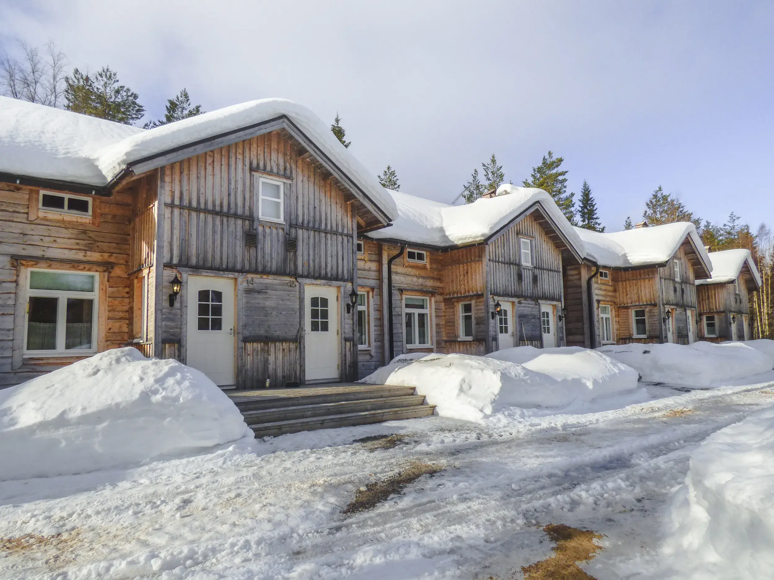 Schneebedeckte Blockhütten der Saija Lodge in der winterlichen Landschaft von Finnisch Lappland an einem sonnigen Tag.
