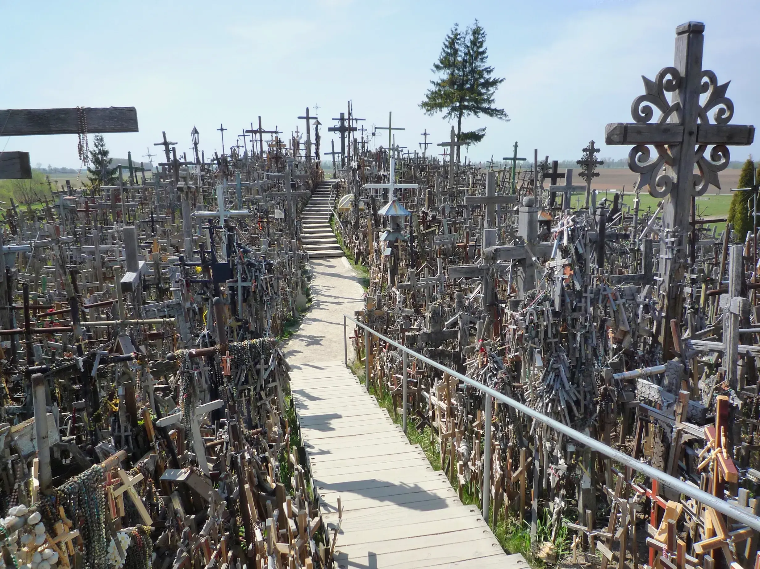 Ein Holzsteg führt durch die beeindruckende Ansammlung unzähliger Kreuze am Wallfahrtsort Berg der Kreuze in Litauen.