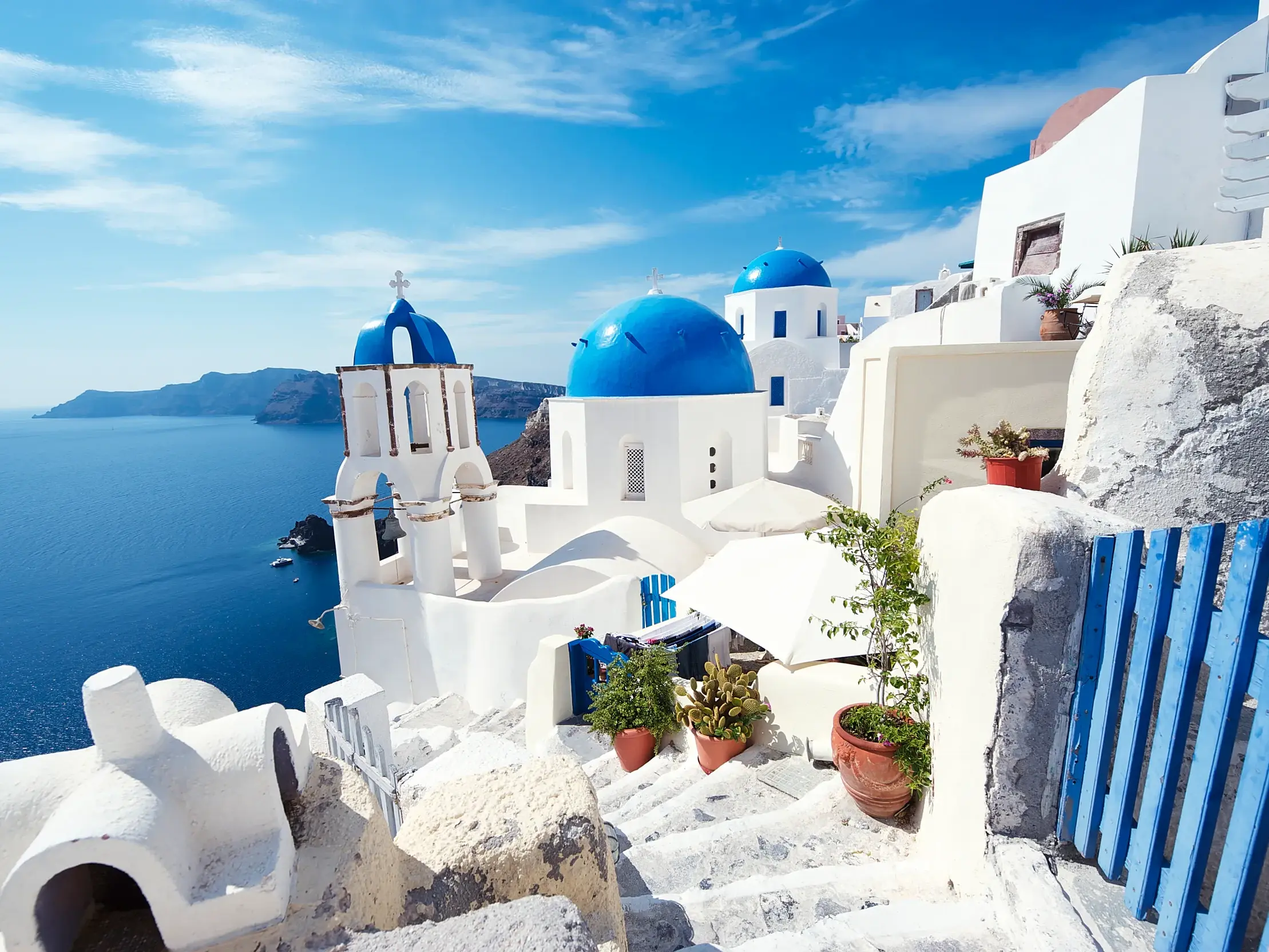 Weiße Kirche mit blauer Kuppel und Glockenturm auf der Kykladeninsel Santorin mit Blick auf die tiefblaue Ägäis.