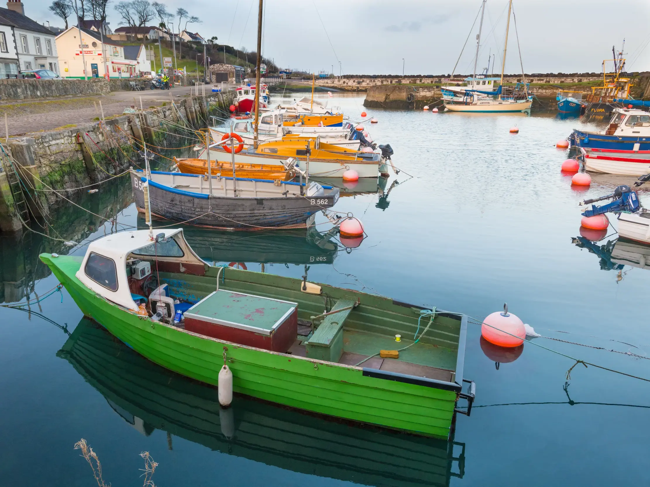 Ein leuchtend grünes Fischerboot liegt neben anderen Booten im malerischen Hafen von Ballycastle in Nordirland.