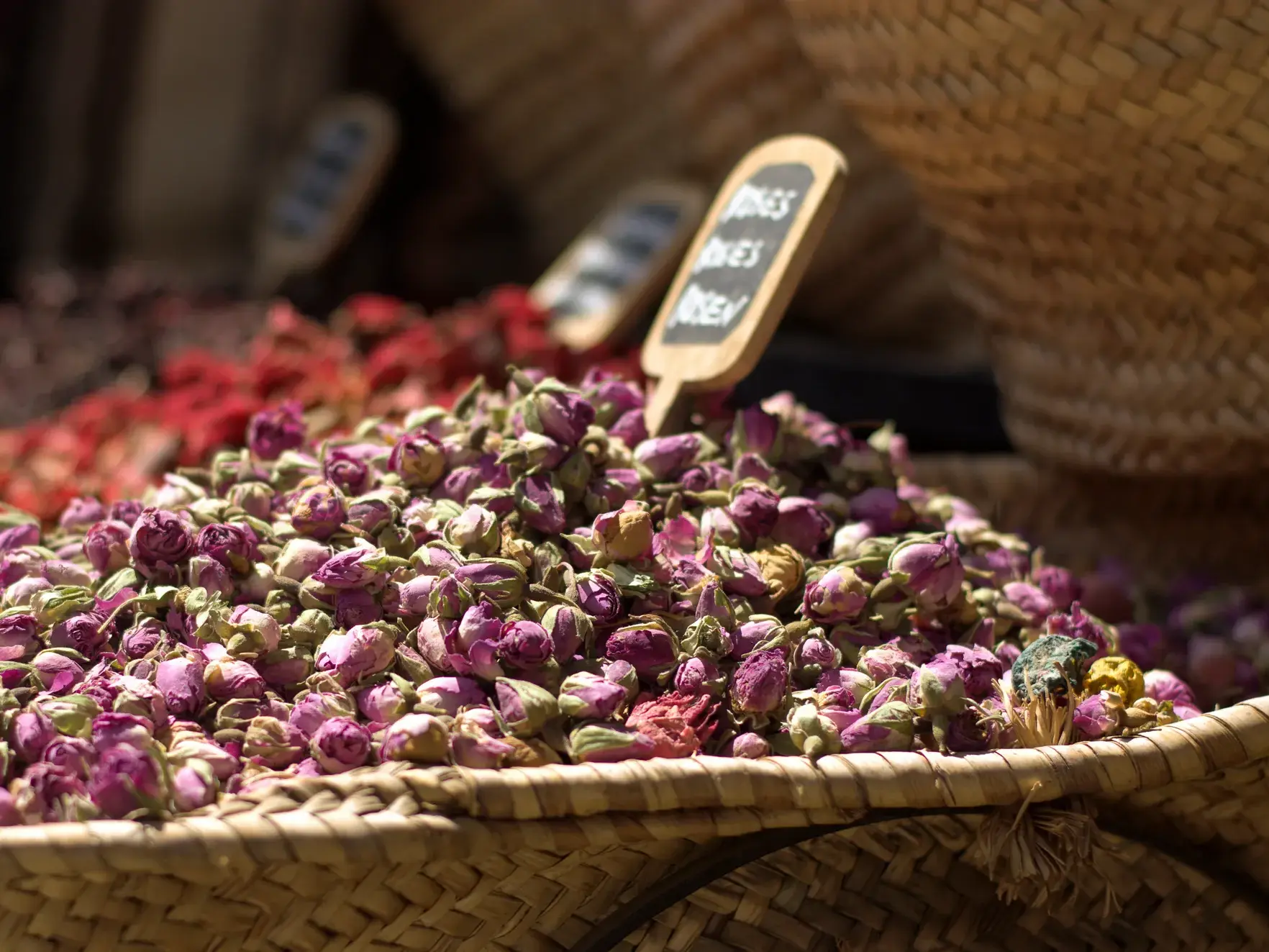 Nahaufnahme von getrockneten Rosenknospen in einem geflochtenen Korb auf einem bunten Gewürzmarkt in Amman, Jordanien.
