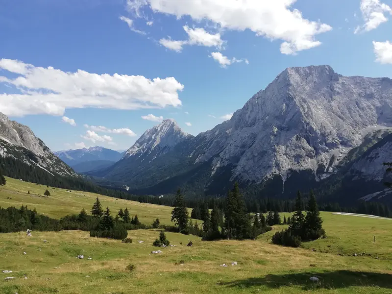 Panoramablick auf die felsigen Gipfel der Mieminger Berge in Tirol über ein grünes Tal mit sanften Almwiesen bei Sonnenschein.