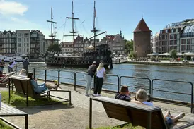 Menschen entspannen an der Uferpromenade der Mottlau in Danzig und genießen bei Sonnenschein den Blick auf ein historisches Schiff.