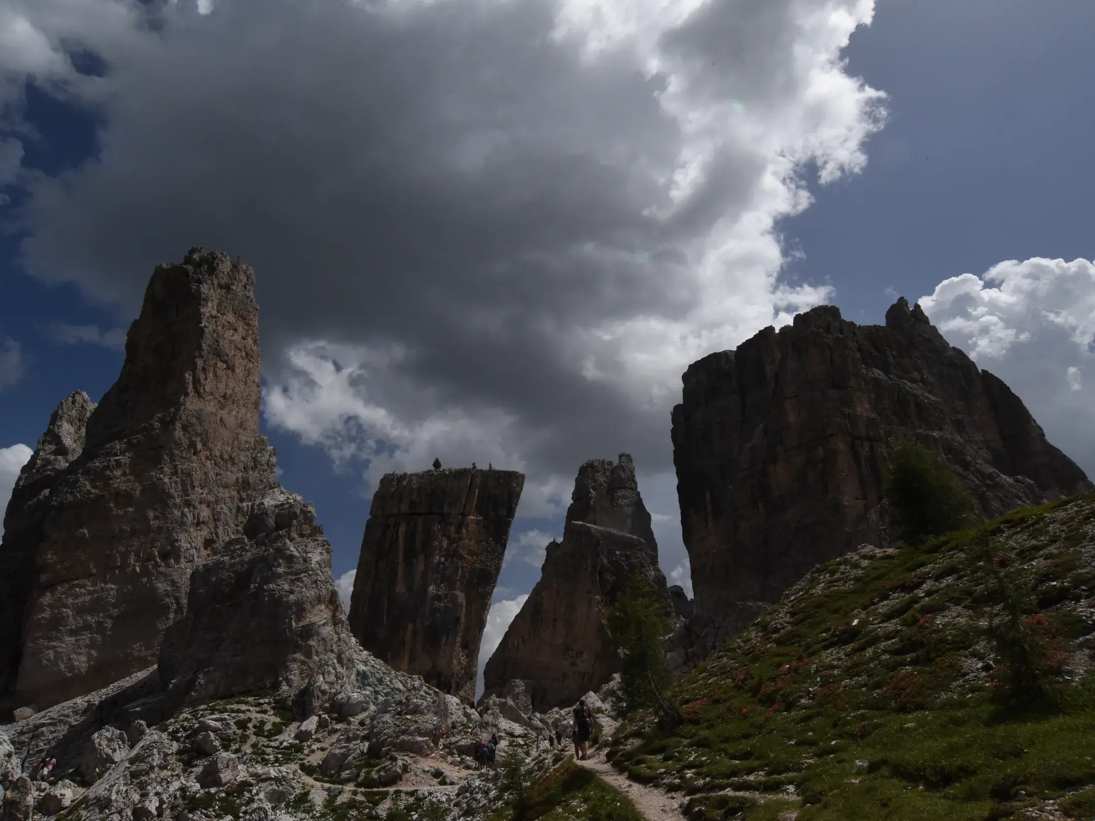 Wanderer auf dem Höhenweg Alta Via 1 mit Blick auf die markanten Felstürme der Cinque Torri bei dramatischem Himmel.