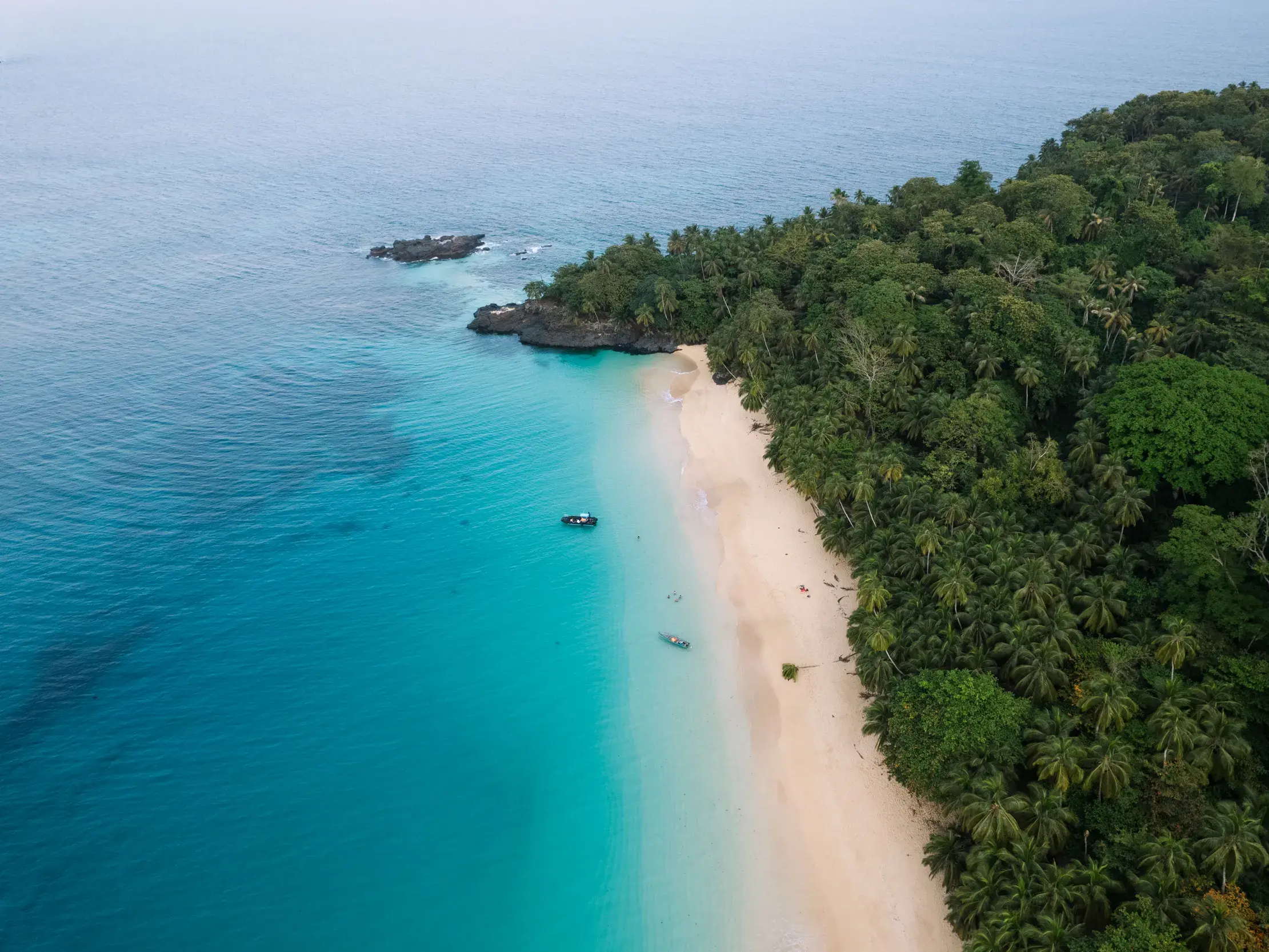 Luftaufnahme eines einsamen Sandstrandes auf São Tomé, gesäumt von üppigem Regenwald und dem türkisfarbenen Atlantik.