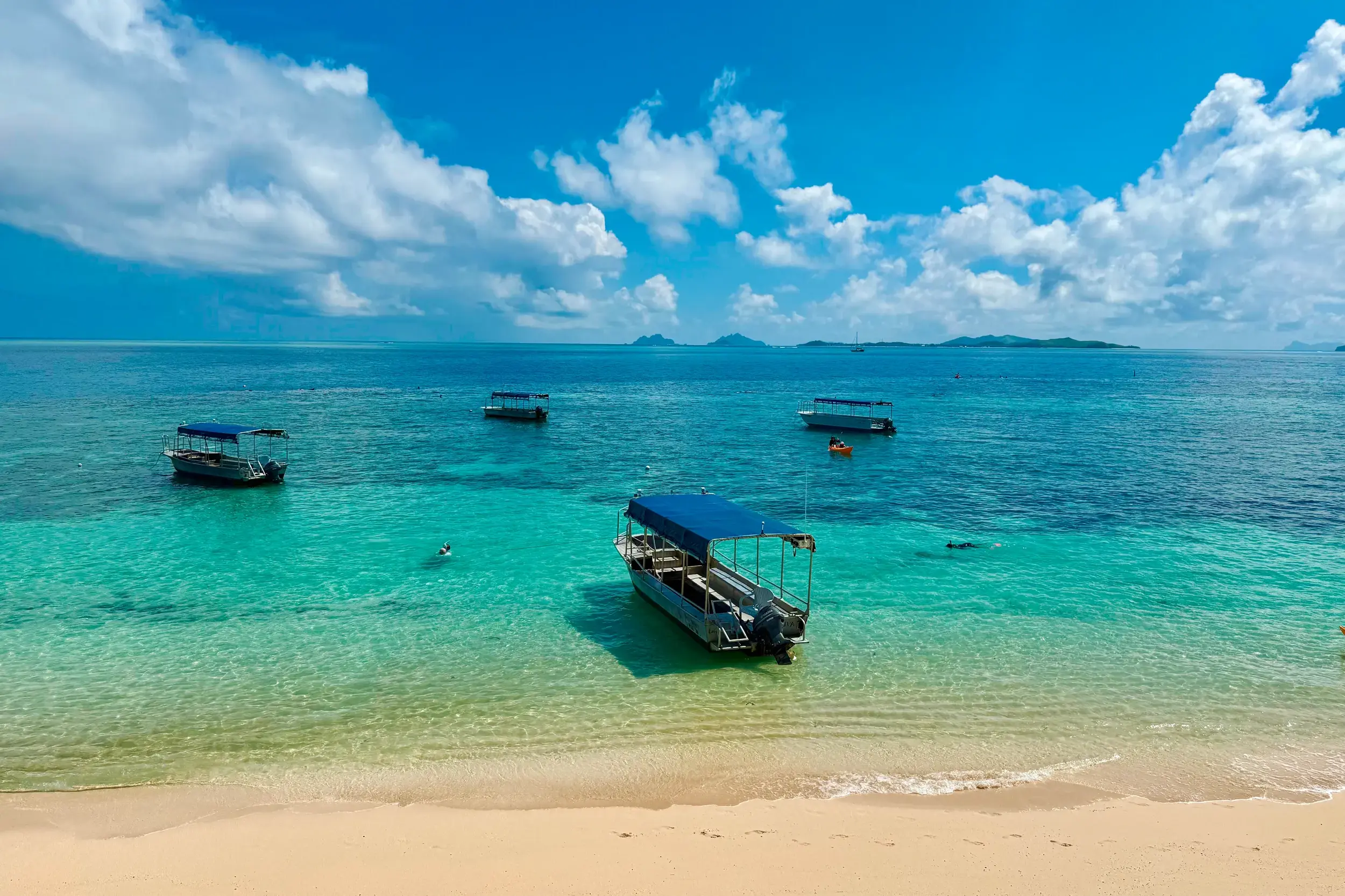 Ausflugsboote mit blauem Dach ankern in der türkisfarbenen Lagune der Mamanuca-Inseln auf Fiji unweit des Sandstrandes.