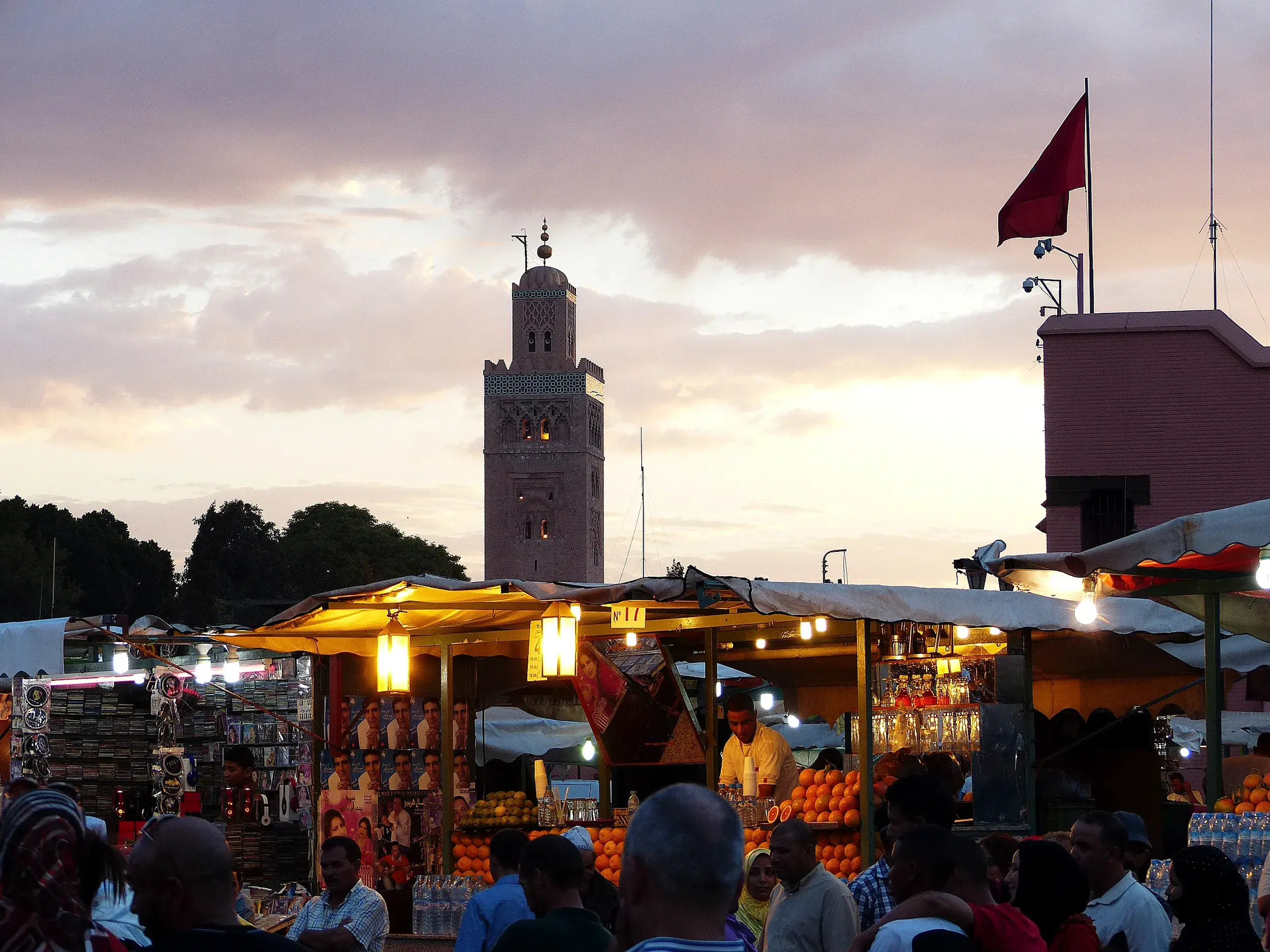 Menschenmenge an beleuchteten Marktständen auf dem Djemaa el-Fna bei Dämmerung, im Hintergrund das Minarett der Koutoubia-Moschee.