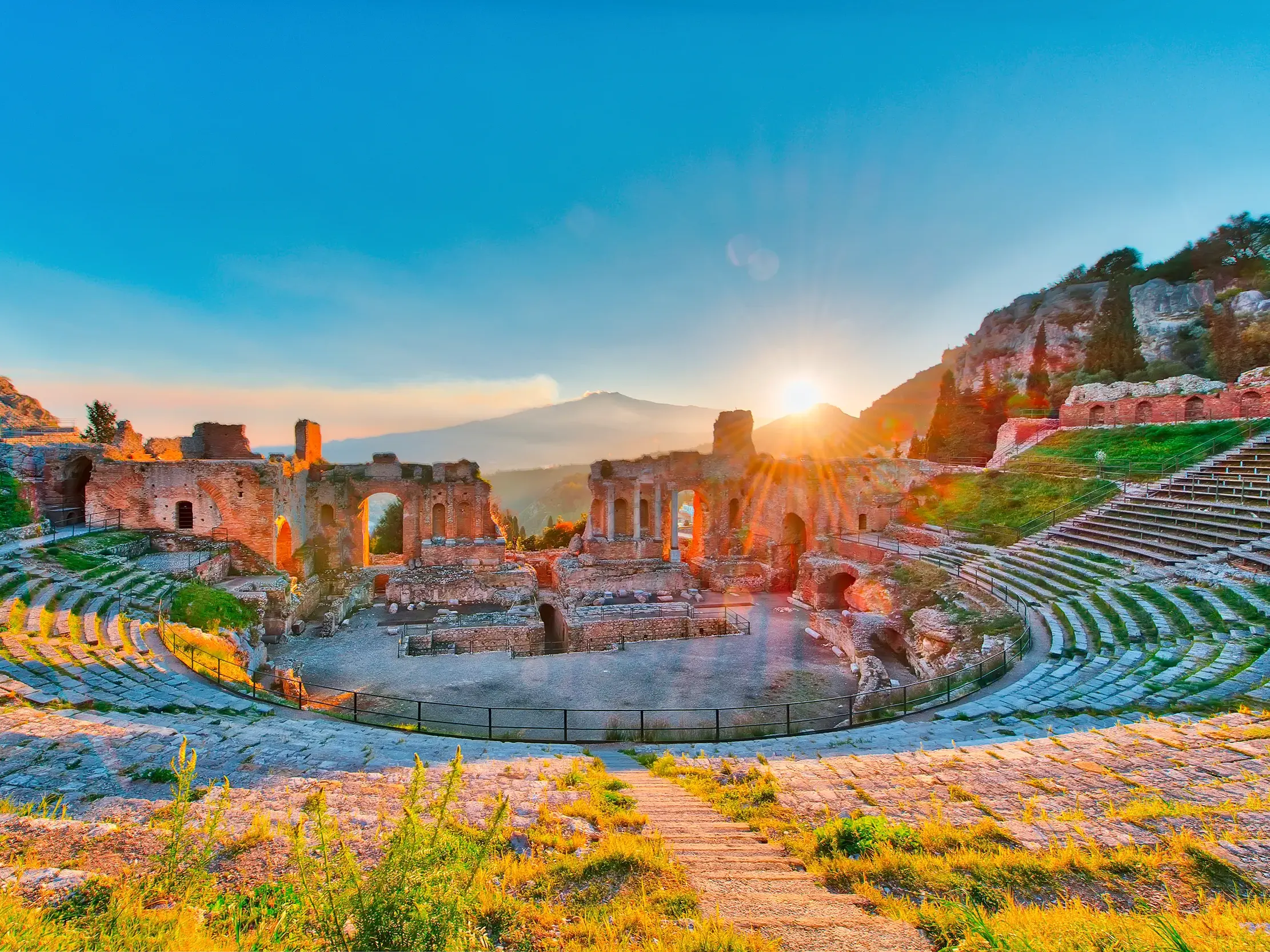 Das antike griechisch-römisches Theater in Taormina bei Sonnenaufgang, mit malerischem Blick auf den rauchenden Vulkan Ätna.