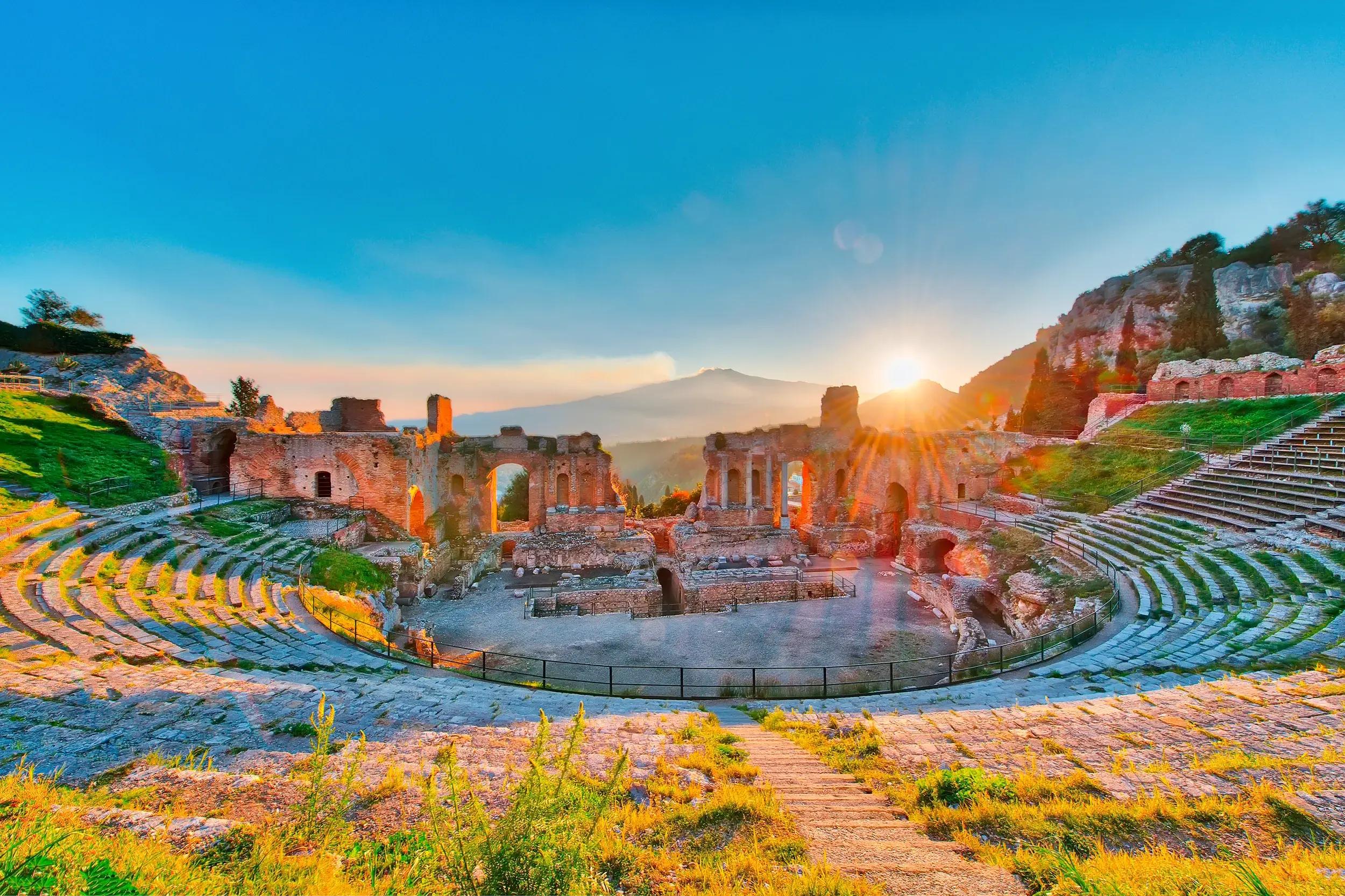 Das antike griechisch-römisches Theater in Taormina bei Sonnenaufgang, mit malerischem Blick auf den rauchenden Vulkan Ätna.