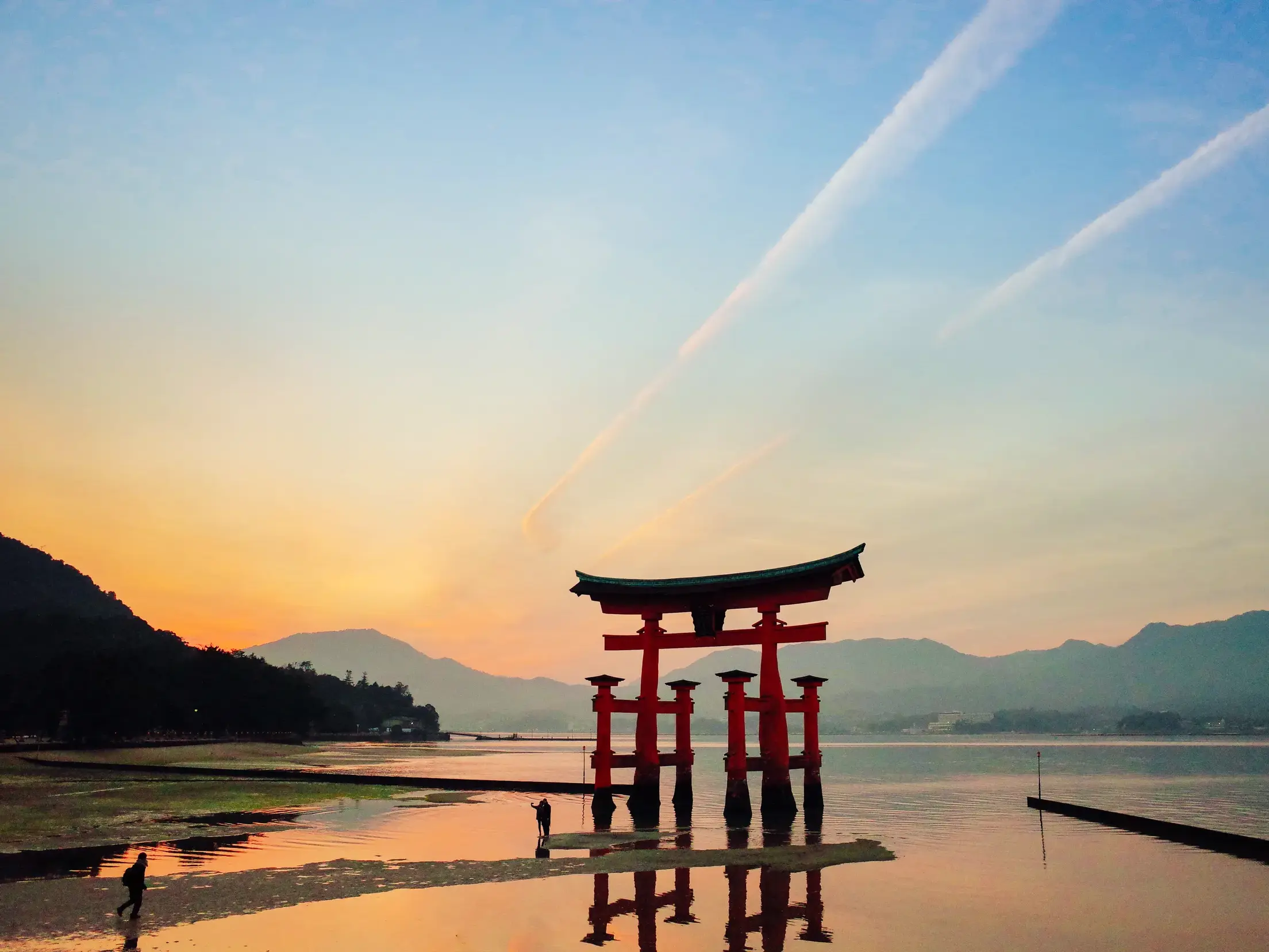 Das rote Torii des Itsukushima-Schreins auf der Insel Miyajima, das sich bei Sonnenuntergang im ruhigen Wasser der Bucht spiegelt.