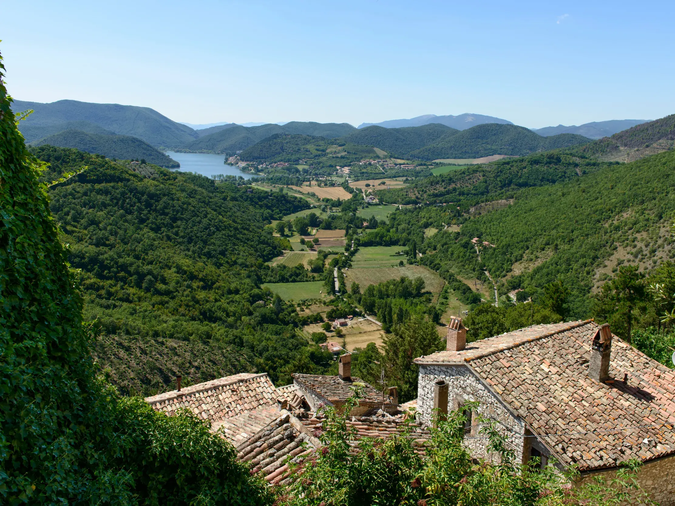 Blick über die Ziegeldächer des Bergdorfs Labro auf den malerischen Piediluco-See in der grünen Hügellandschaft Umbriens.