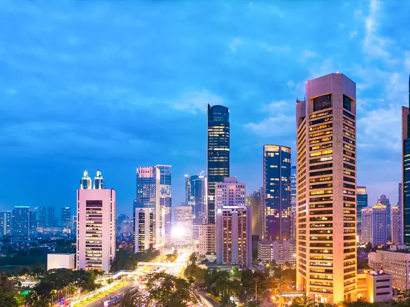 Moderne Wolkenkratzer der Megacity Jakarta ragen bei Dämmerung in den blauen Himmel über beleuchteten Straßen.