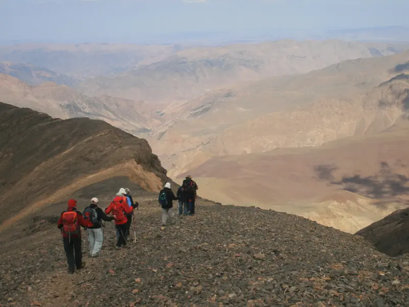 Eine Hauser-Trekkinggruppe wandert auf dem steinigen Gipfelgrat des Djebel Mgoun mit Panoramablick über den Hohen Atlas Marokkos.