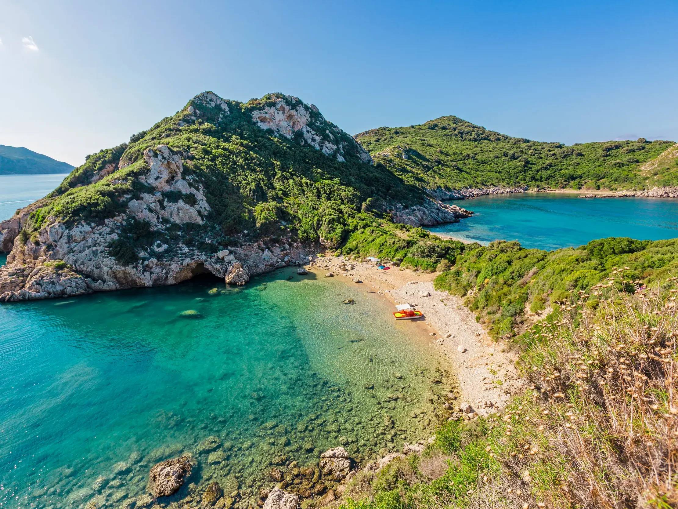 Malerische Doppelbucht bei Agios Georgios auf Korfu mit kristallklarem, türkisfarbenem Meer und üppig grünen, felsigen Hängen.