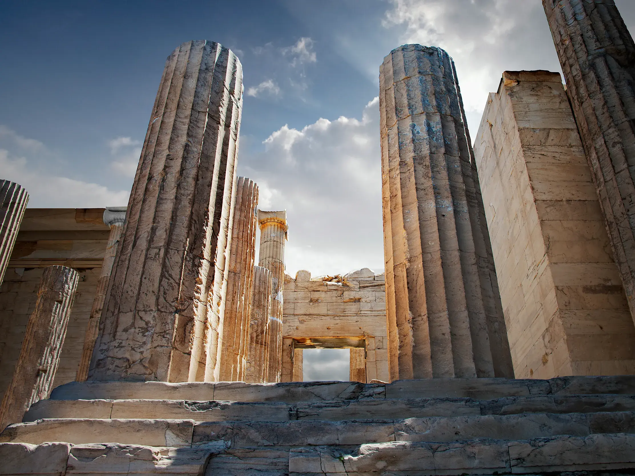 Monumentale Säulen eines antiken Tempels auf der Akropolis in Athen, von unten fotografiert gegen den sonnigen Himmel.