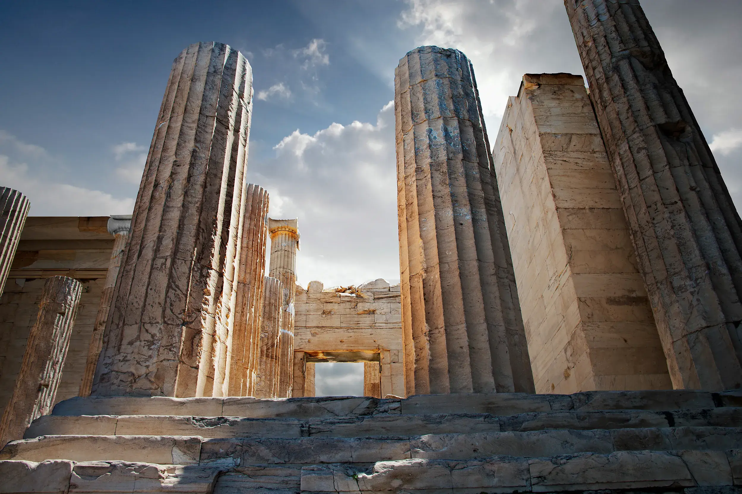 Monumentale Säulen eines antiken Tempels auf der Akropolis in Athen, von unten fotografiert gegen den sonnigen Himmel.