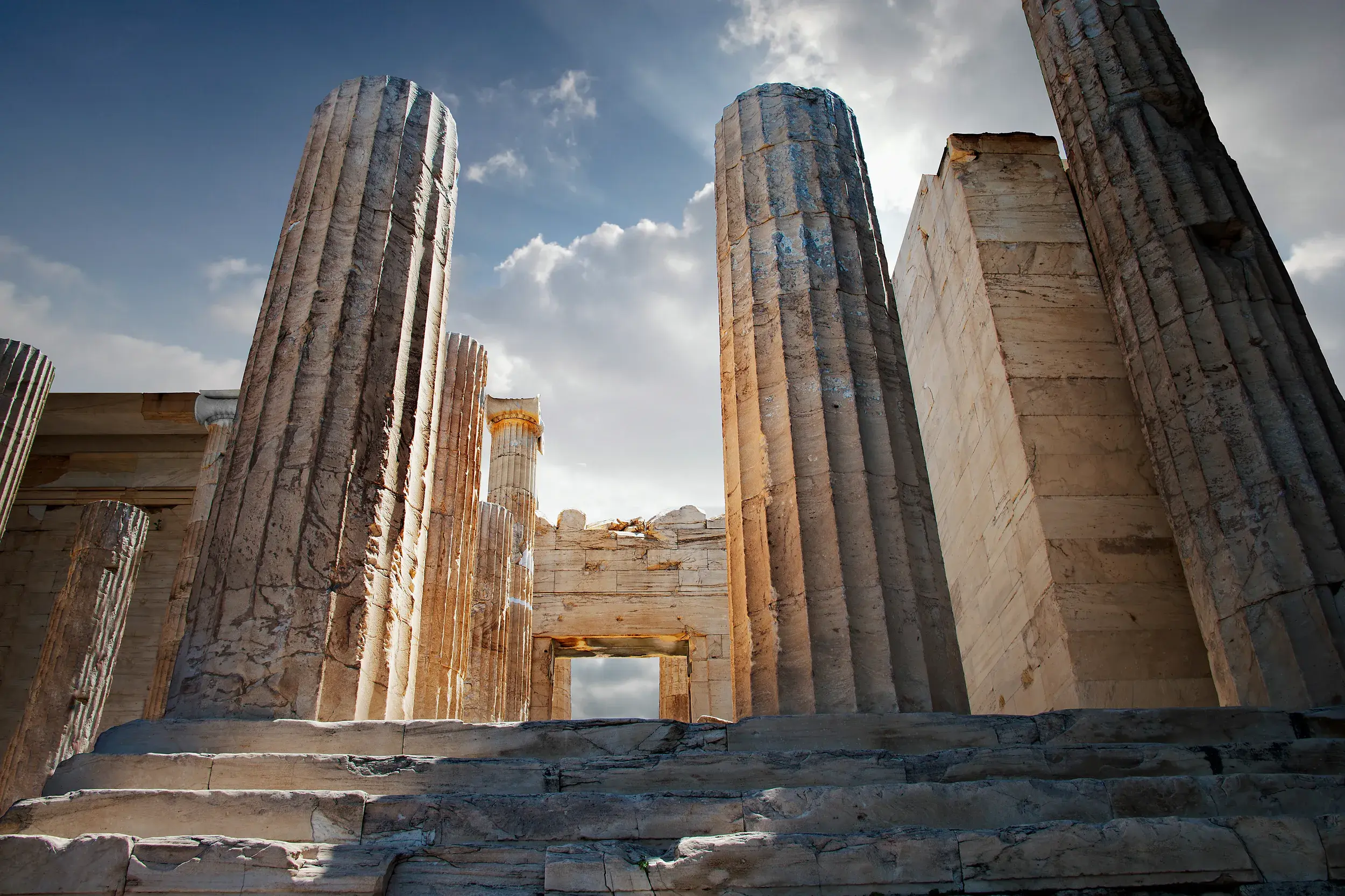 Monumentale Säulen eines antiken Tempels auf der Akropolis in Athen, von unten fotografiert gegen den sonnigen Himmel.