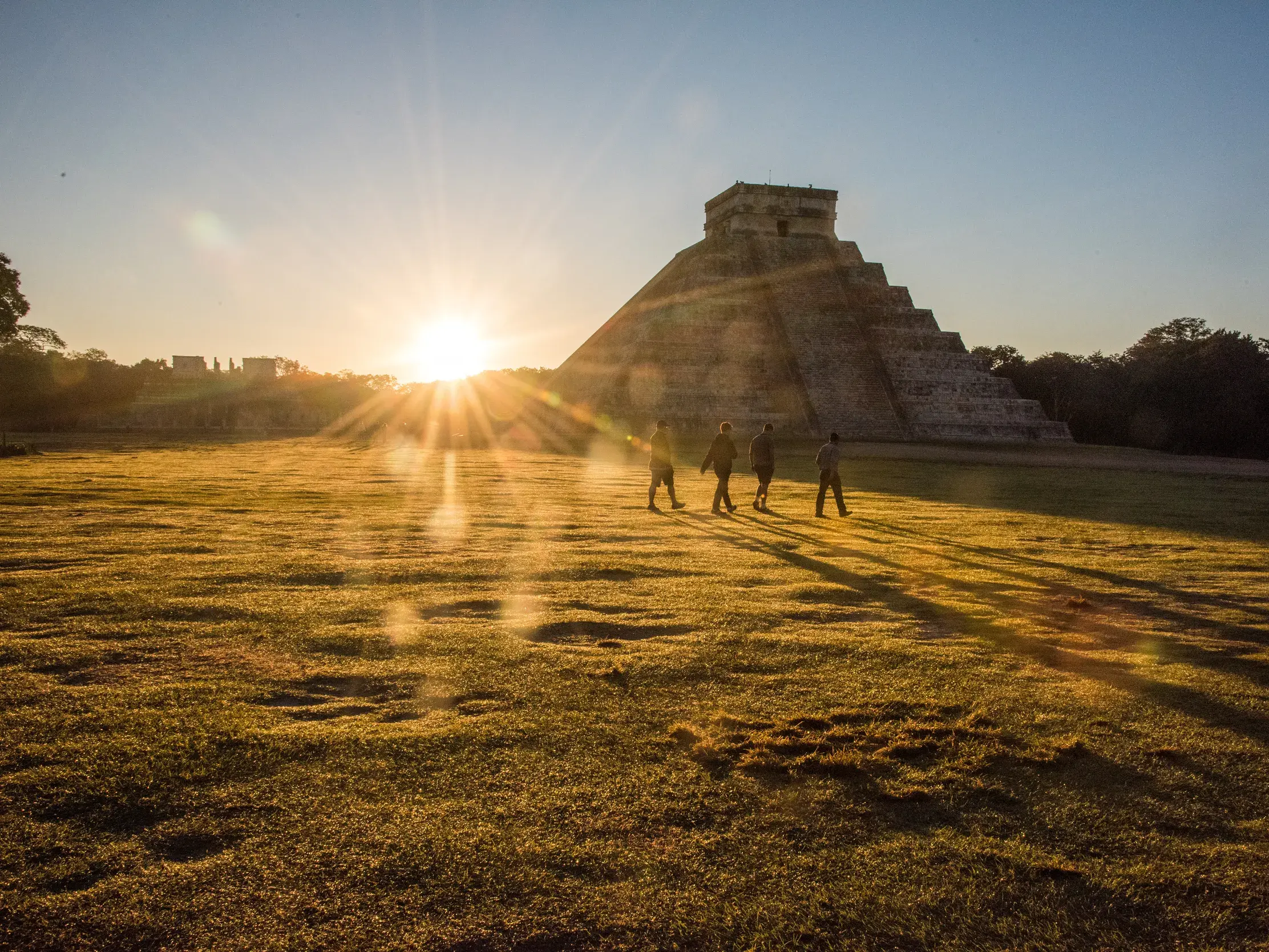 Eine kleine Reisegruppe spaziert bei Sonnenuntergang zur berühmten Pyramide des Kukulkán in der Maya-Stätte Chichén Itzá in Mexiko.