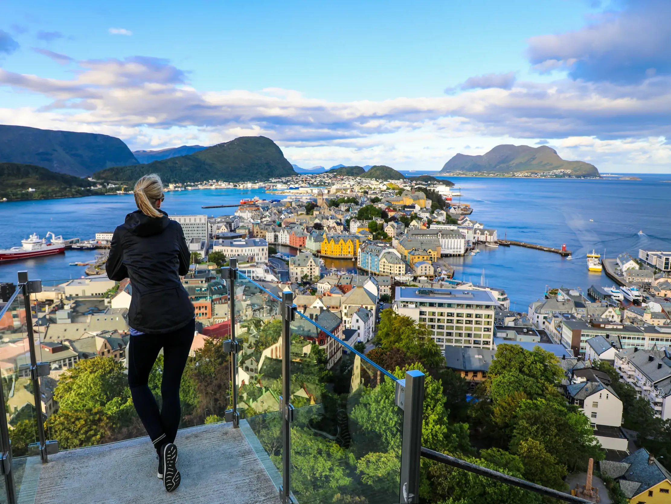 Frau blickt von der Aussichtsplattform Fjellstua auf die farbenfrohen Jugendstilhäuser von Alesund am Fjord in Norwegen.