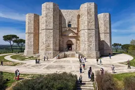 Das imposante, achteckige Castel del Monte in Apulien unter blauem Himmel. Besucher erkunden den Vorplatz des Stauferkastells.