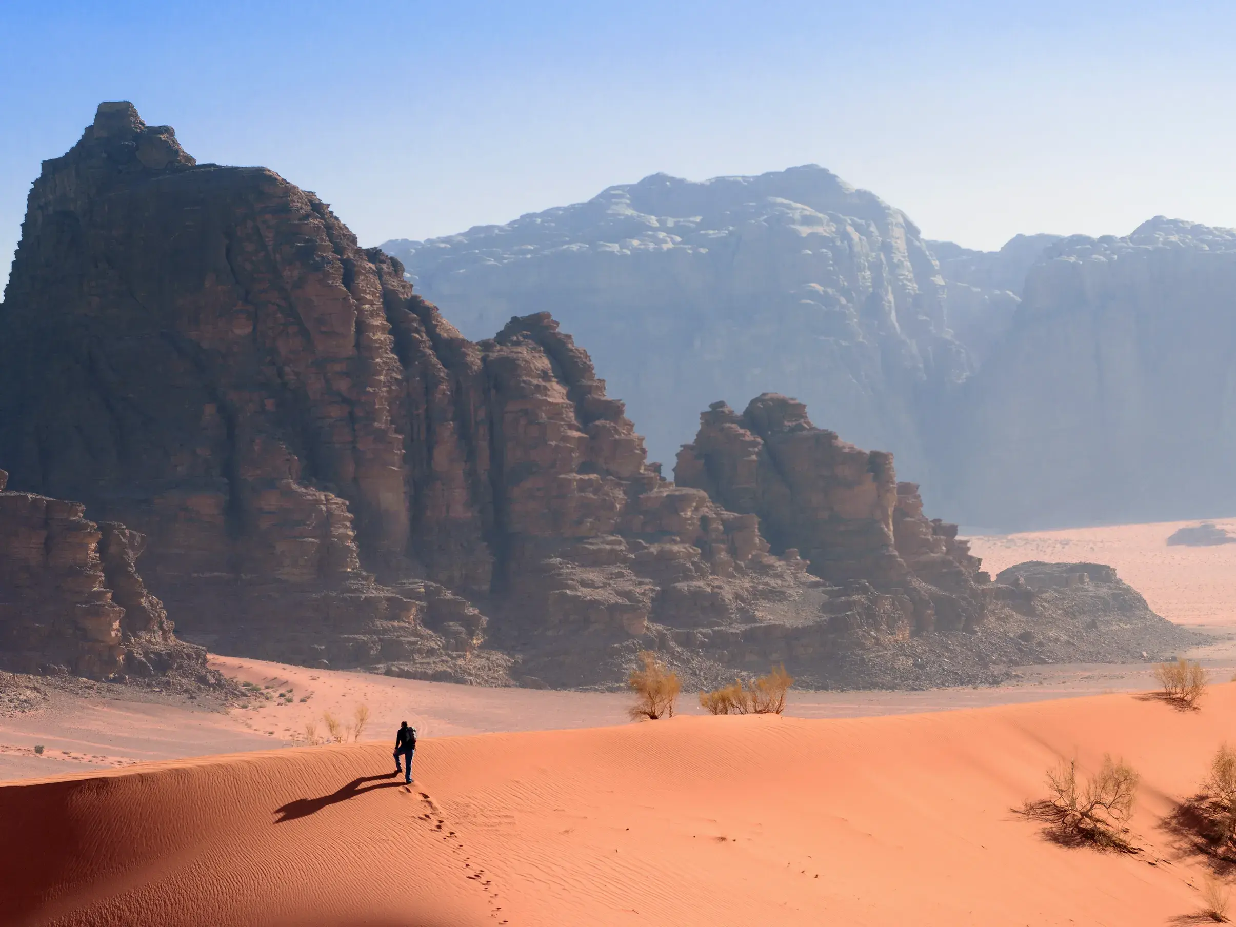 Ein Reisender wandert auf dem Kamm einer orangeroten Sanddüne durch die weite Wüstenlandschaft des Wadi Ram in Jordanien.