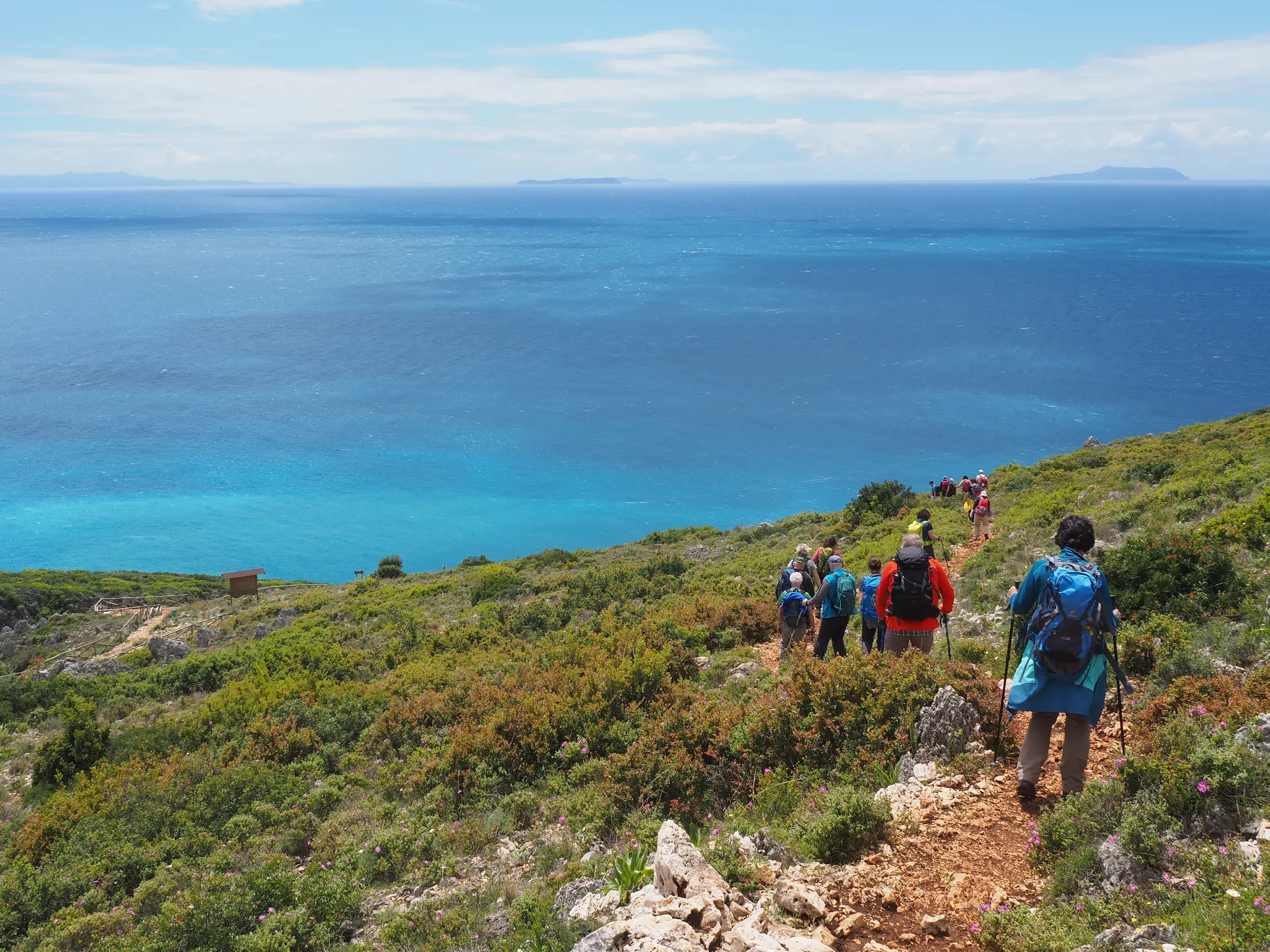 Eine Wandergruppe beim Trekking auf einem Küstenpfad an der Albanischen Riviera mit weitem Blick über das tiefblaue Ionische Meer.