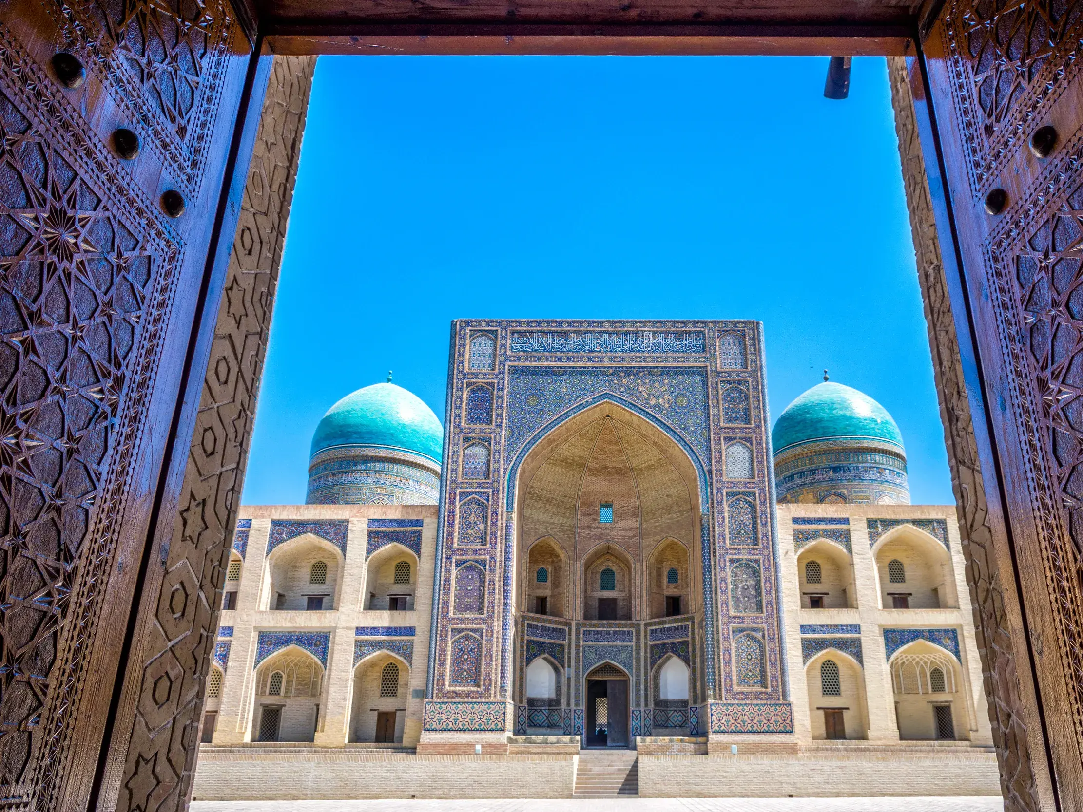 Kunstvoll geschnitzte Holztore geben den Blick frei auf die historische Mir-i-Arab-Medrese in Buchara, Usbekistan.