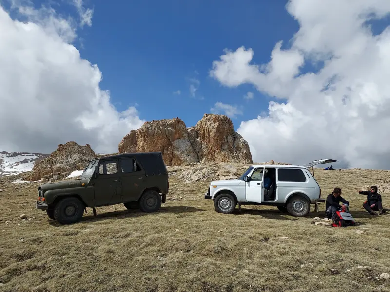 Zwei Wanderer rasten neben ihren Geländewagen auf einer Hochebene während einer Trekkingreise im Großen Kaukasus.